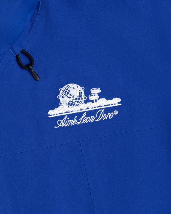 Close-up of a blue Cropped GORE-TEX Shell Jacket with an embroidered white globe logo and Aimé Leon Dore text.