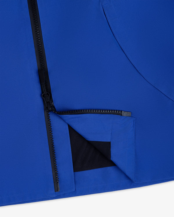 Close-up of a blue Cropped GORE-TEX Shell Jacket with a black front zipper and a partially open bottom hem.