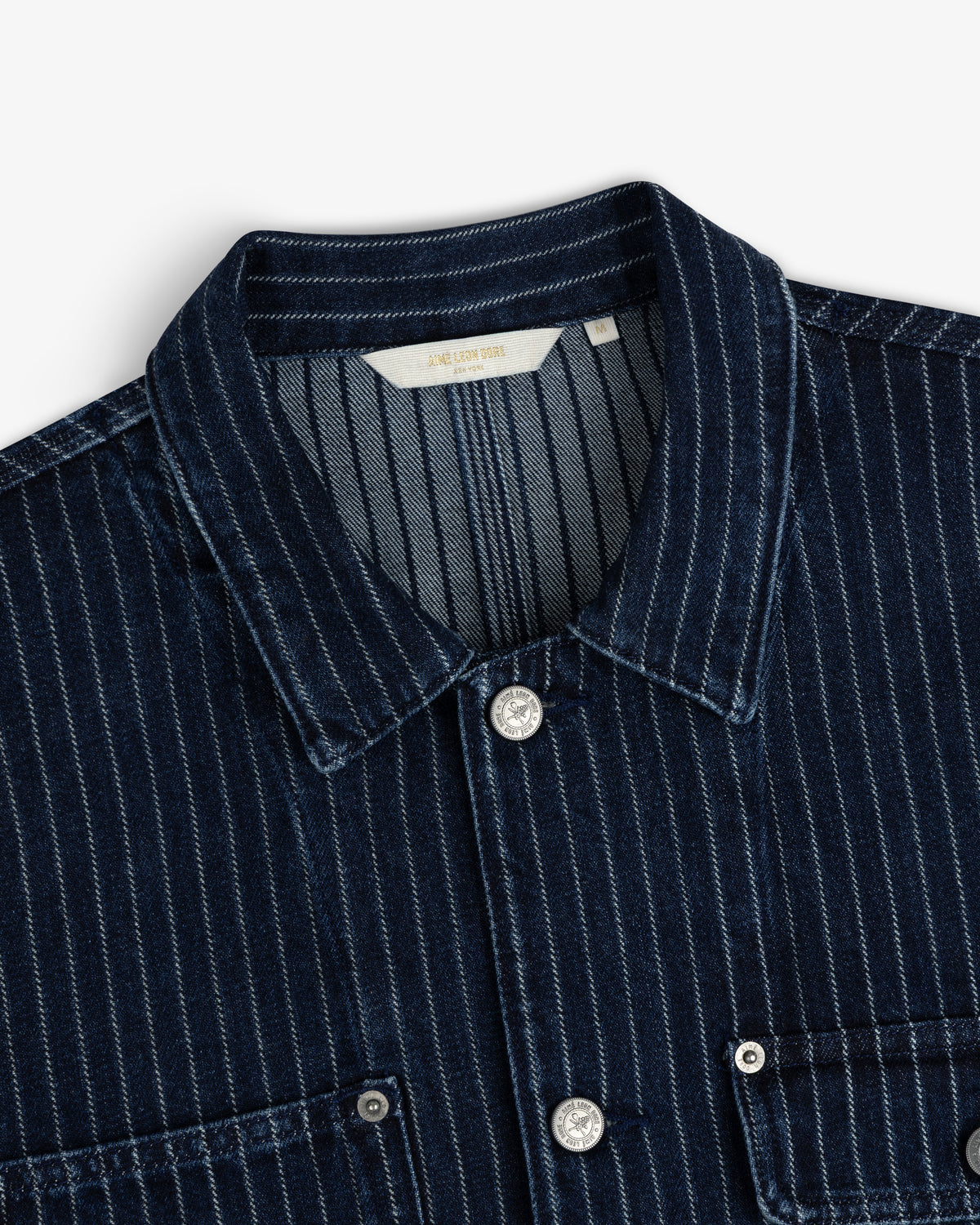 Chalk Stripe Denim Trucker Jacket in dark blue with white stripes, silver buttons, and two front pockets shown close up.