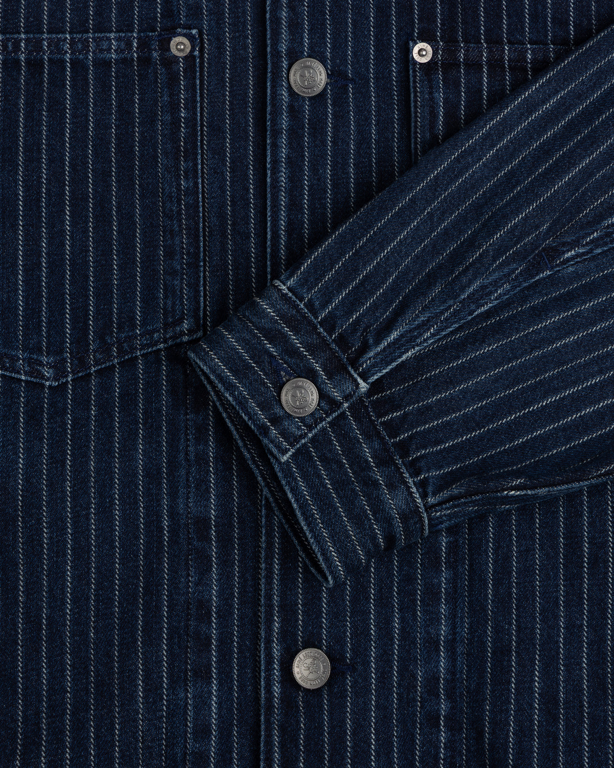 Close-up of the Chalk Stripe Denim Trucker Jacket with silver snap buttons and a folded sleeve.