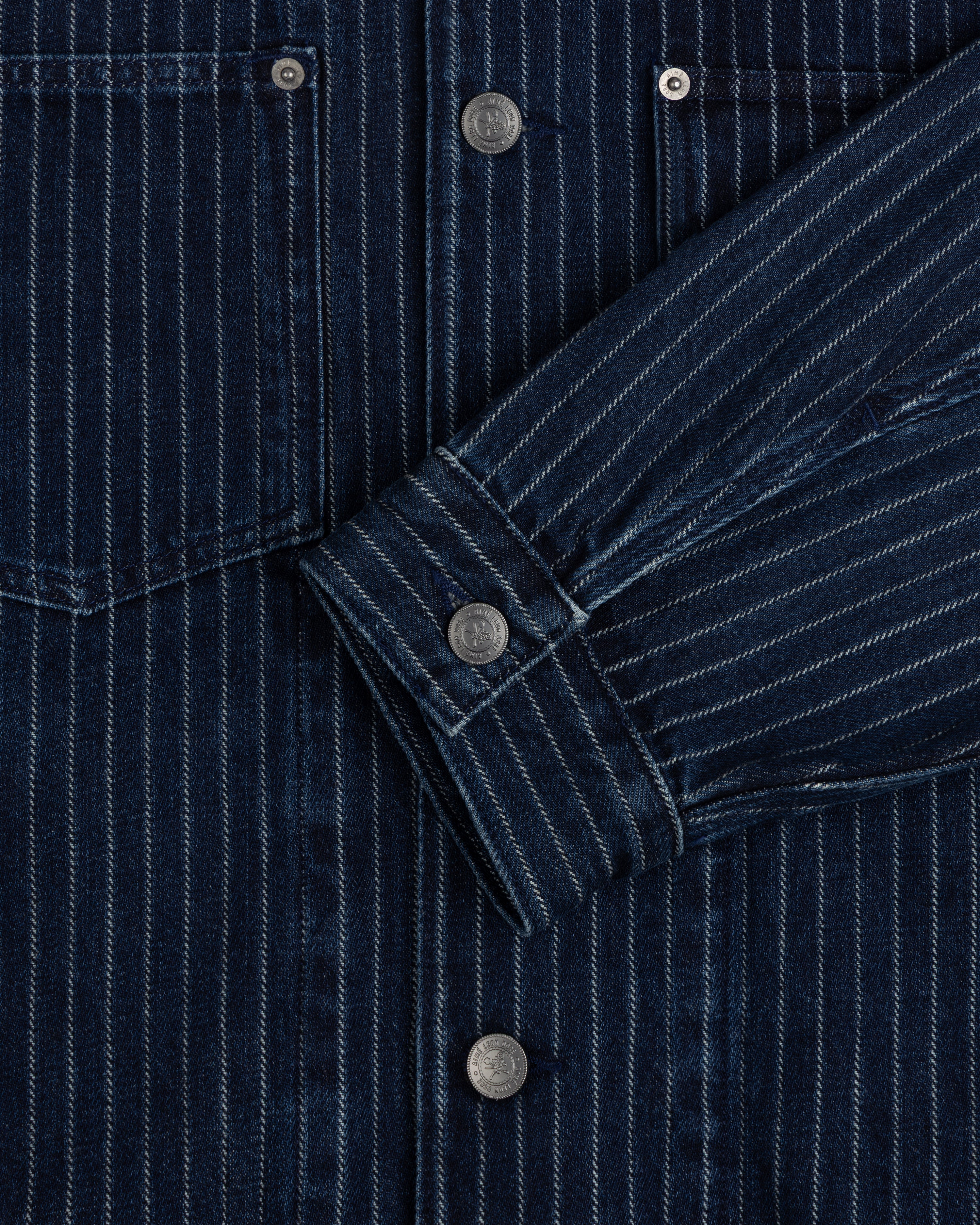 Close-up of the Chalk Stripe Denim Trucker Jacket with silver snap buttons and a folded sleeve.