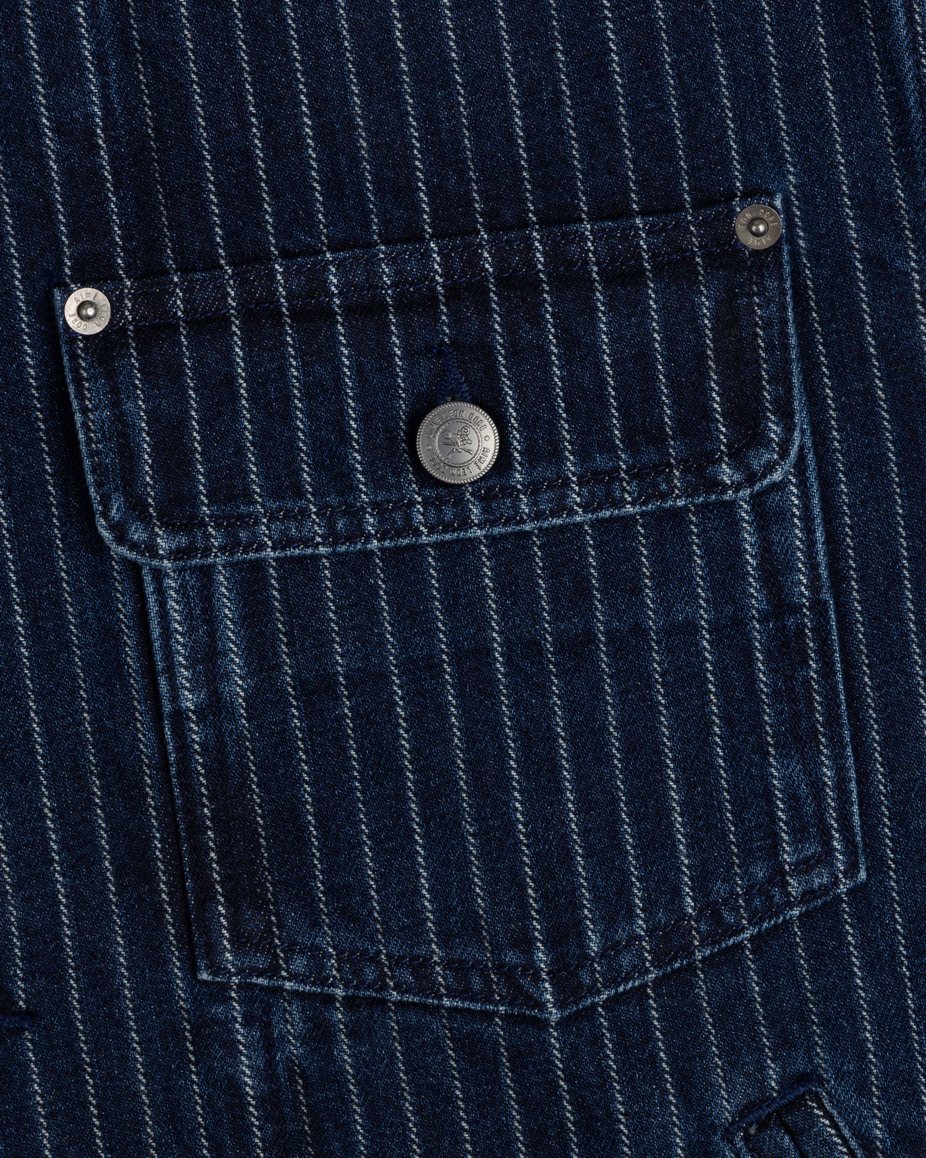 Close-up of Chalk Stripe Denim Trucker Jacket’s blue pocket with white stripes and a metal button on the flap.