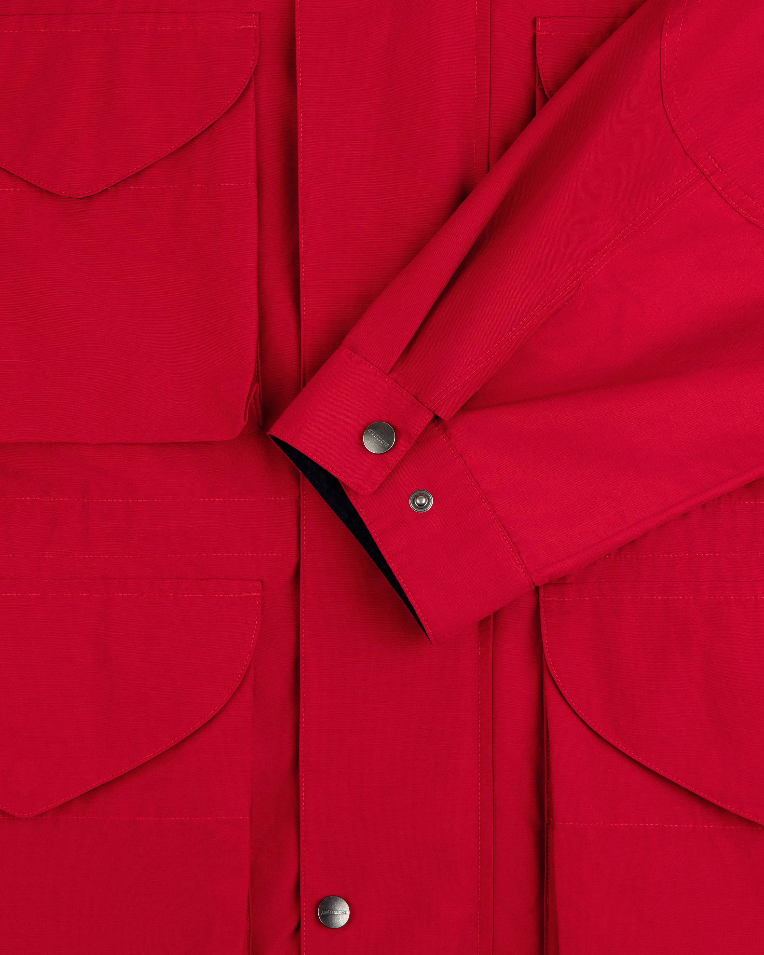 Close-up of the Lightweight Barn Jacket in red, featuring flap pockets, snap buttons, and a crossed sleeve detail.