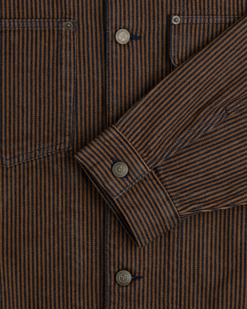 Close-up of a Hickory Stripe Denim Trucker Jacket with brown and navy stripes, metal buttons, pocket, and sleeve.