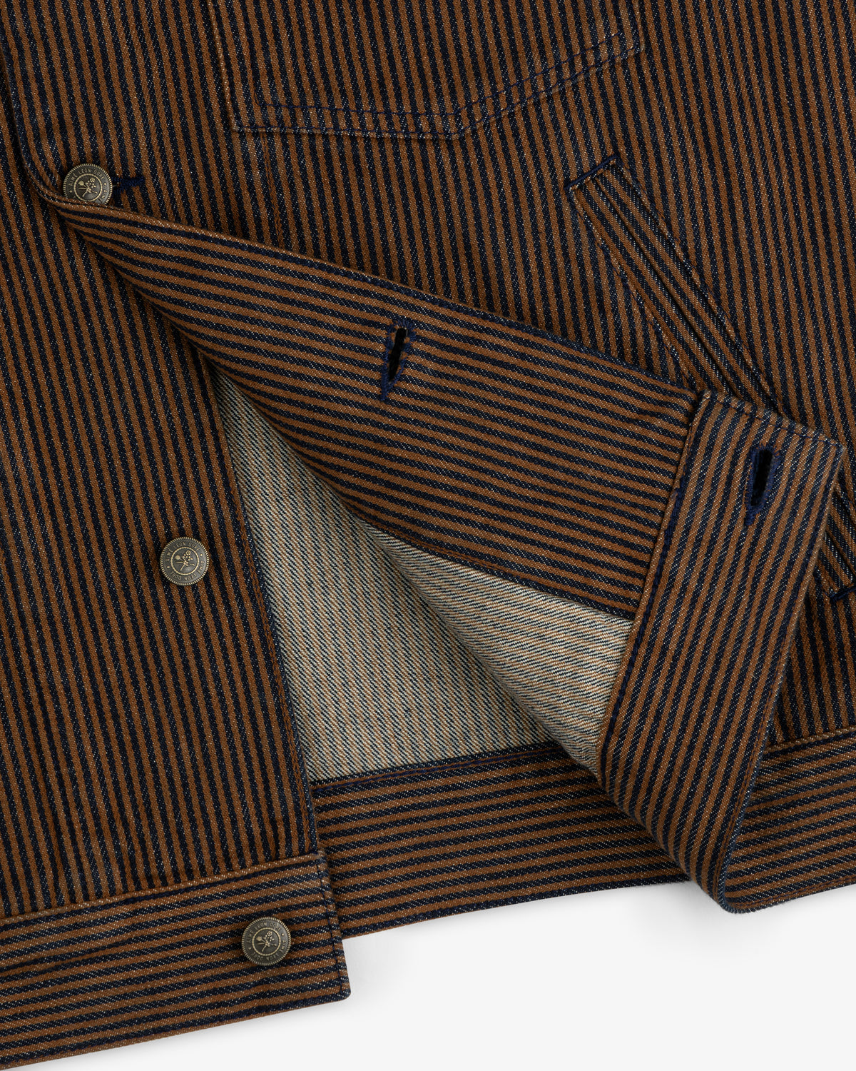 Close-up of the Hickory Stripe Denim Trucker Jacket, featuring brown and navy stripes, buttons, and inner lining.