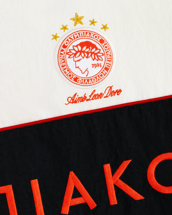 ALD / Olympiacos F.C. Nylon Quarter Zip Pullover in off-white with an embroidered crest and orange lettering on black.