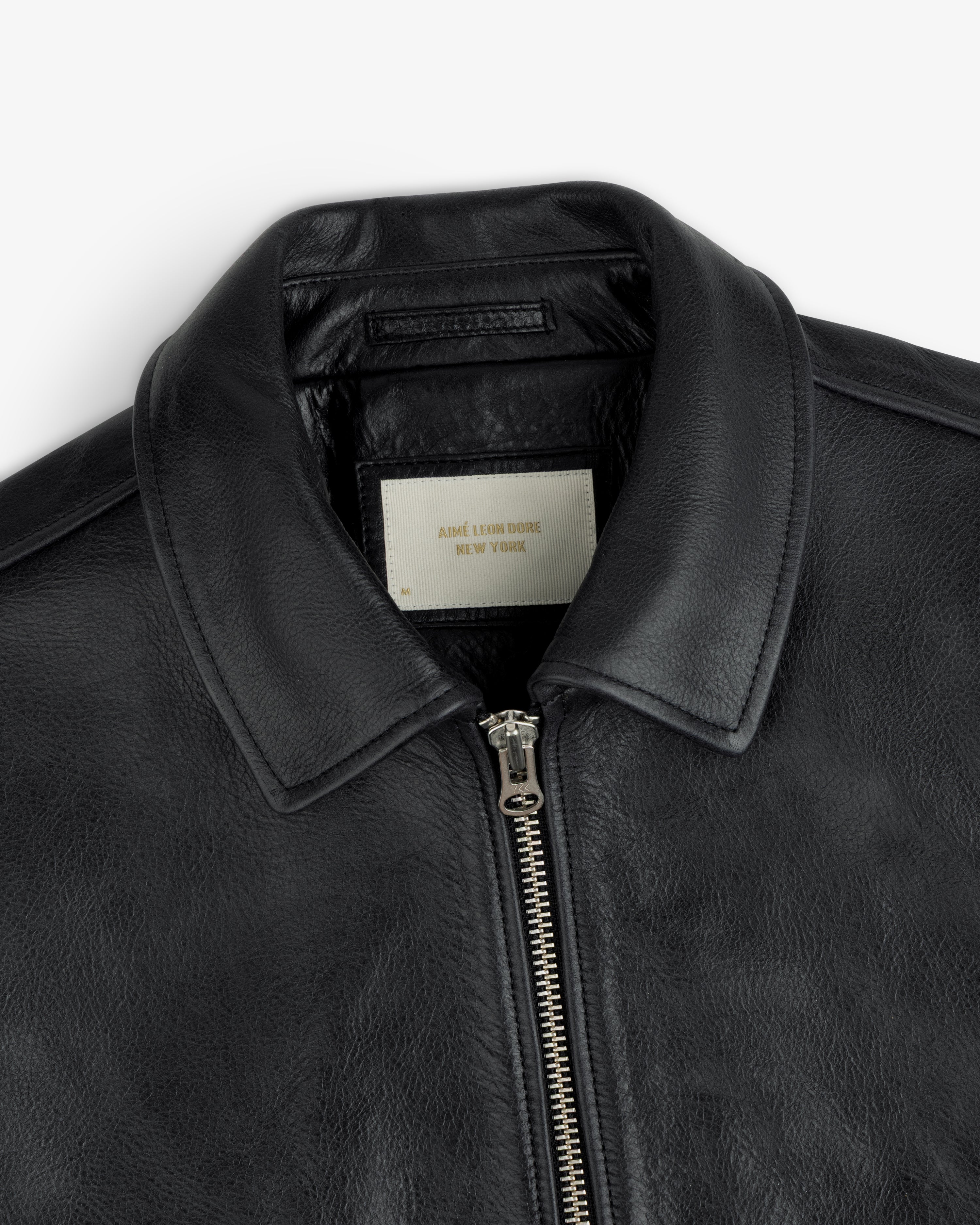 Close-up of a black Napa Leather Bomber Jacket featuring a metal front zipper and a white interior collar tag.
