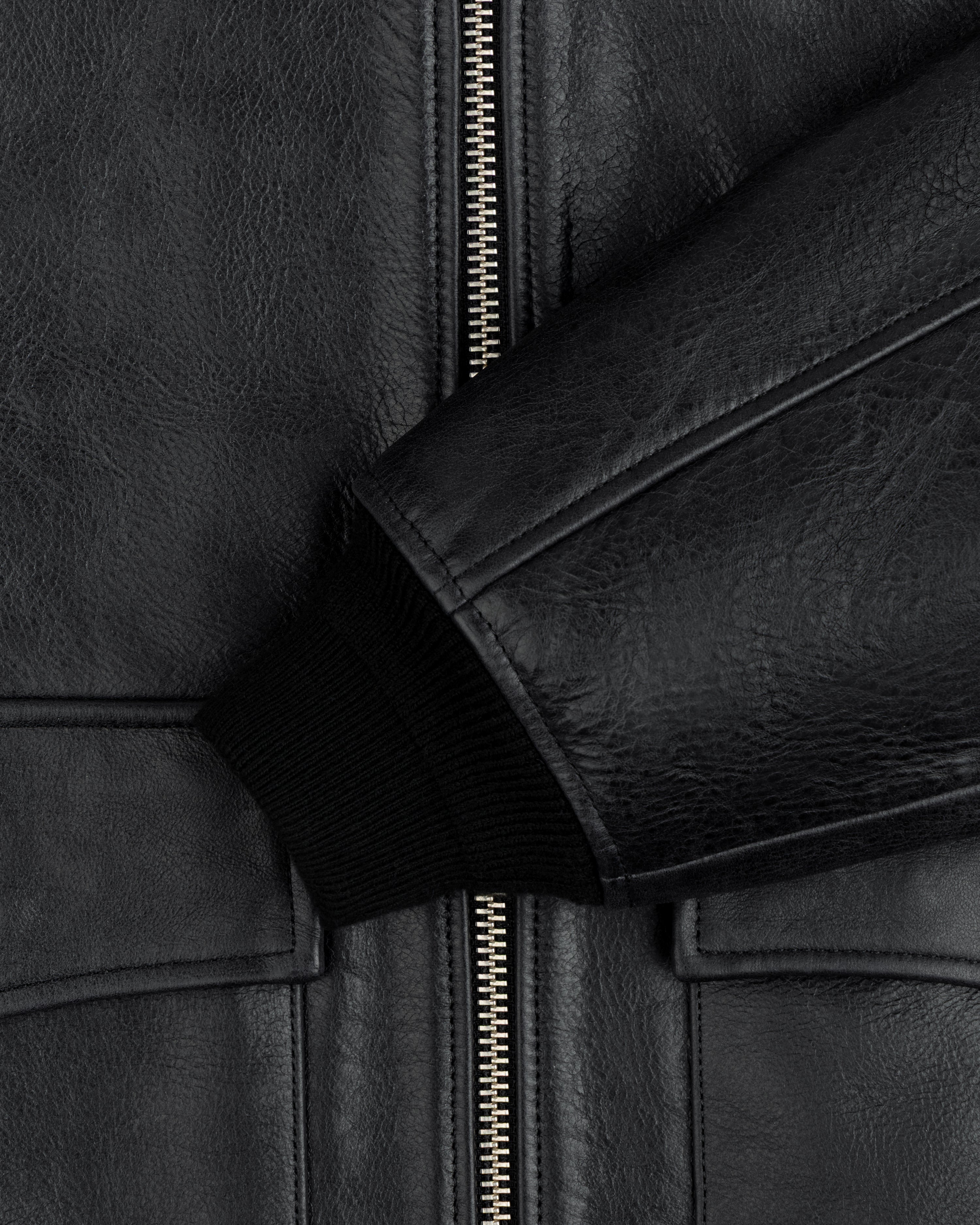 Close-up of a black Napa Leather Bomber Jacket with a central silver zipper and a ribbed knit cuff.