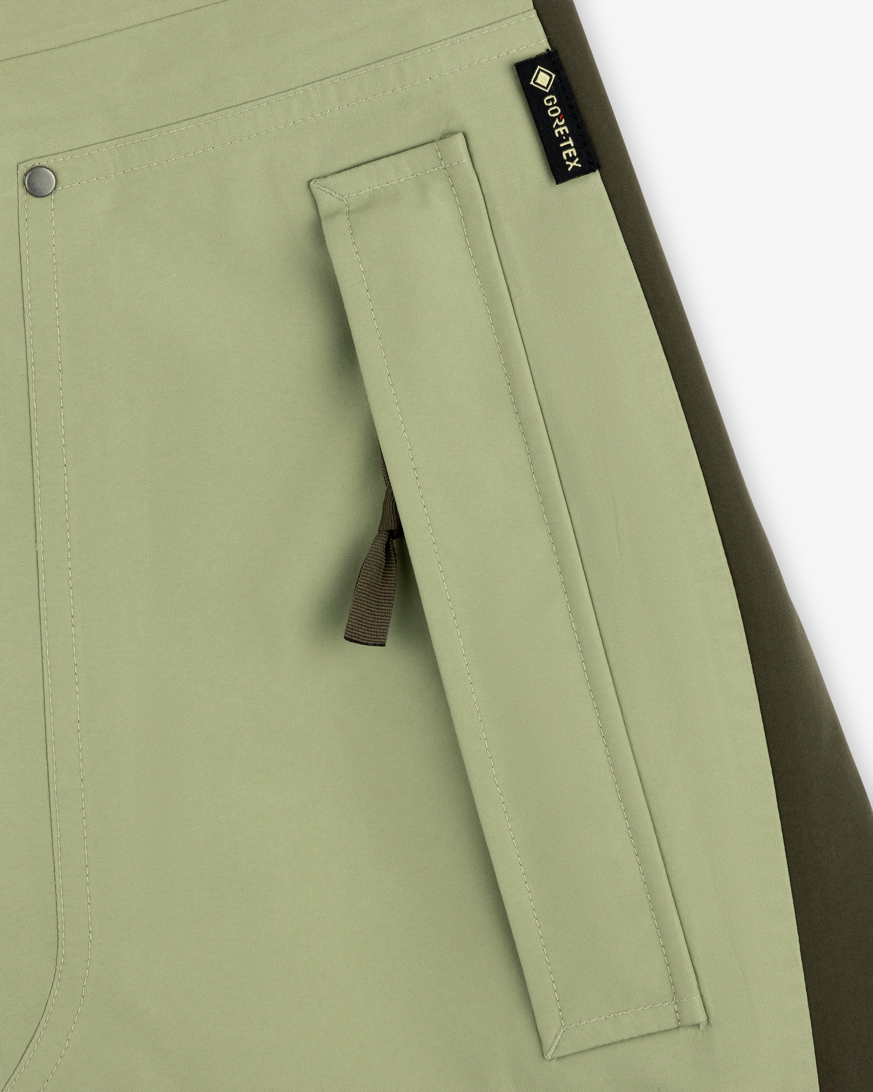 Close-up of ALD / The North Face GORE-TEX Pant pocket in light green with black zipper pull and olive side panel.