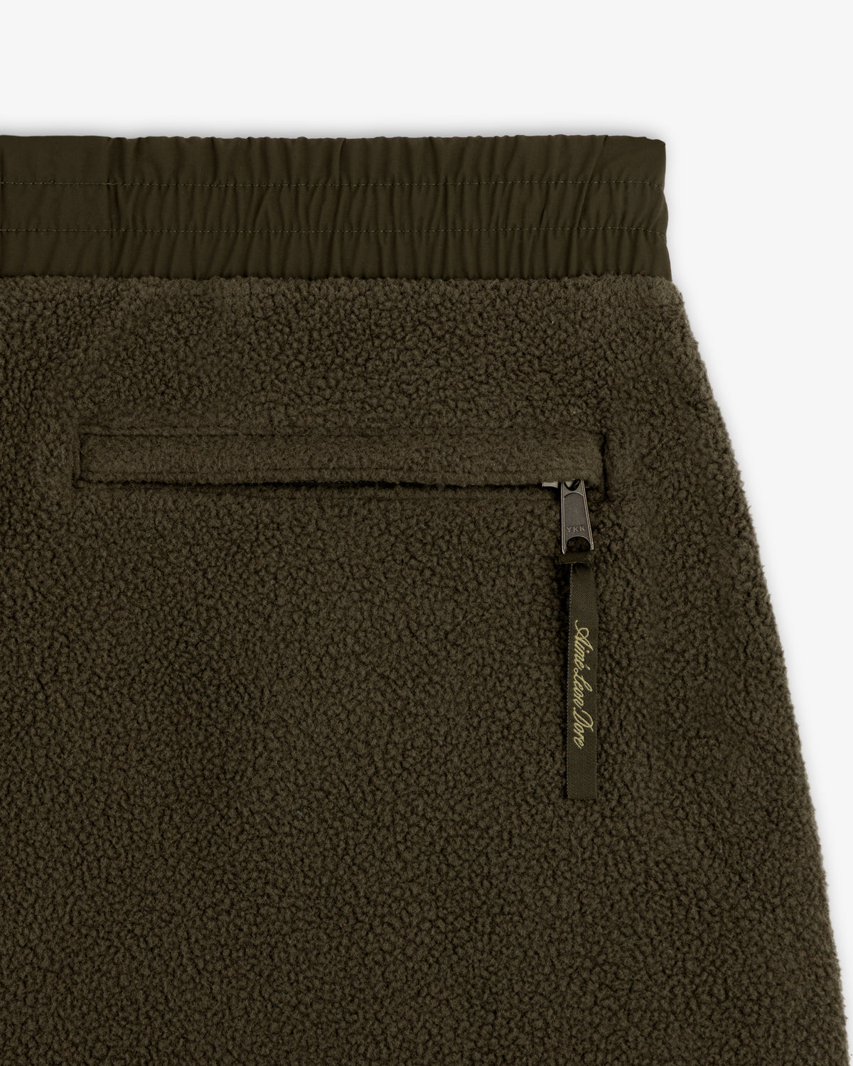 Close-up of ALD / The North Face Denali Fleece Pant in olive green with zippered pocket and elastic waistband.
