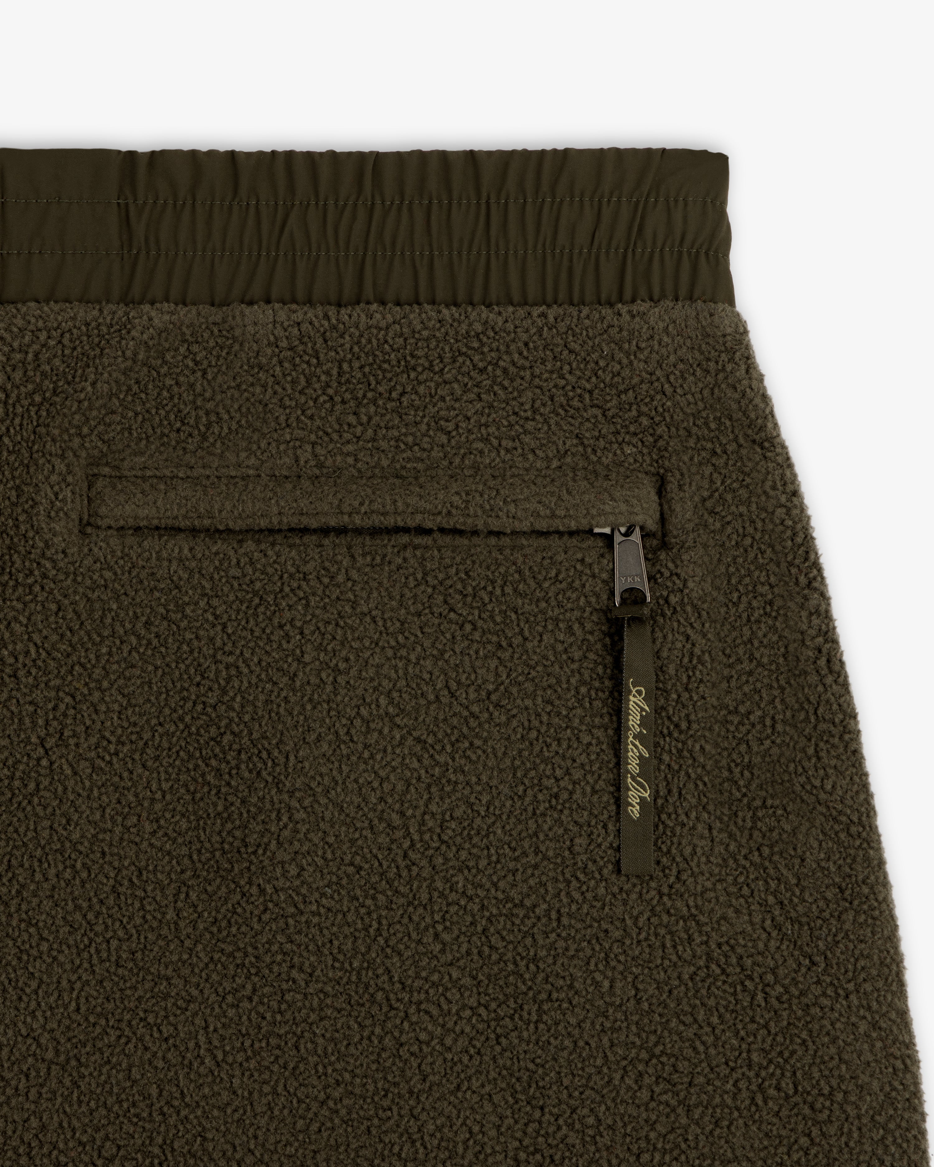 Close-up of ALD / The North Face Denali Fleece Pant in olive green with zippered pocket and elastic waistband.