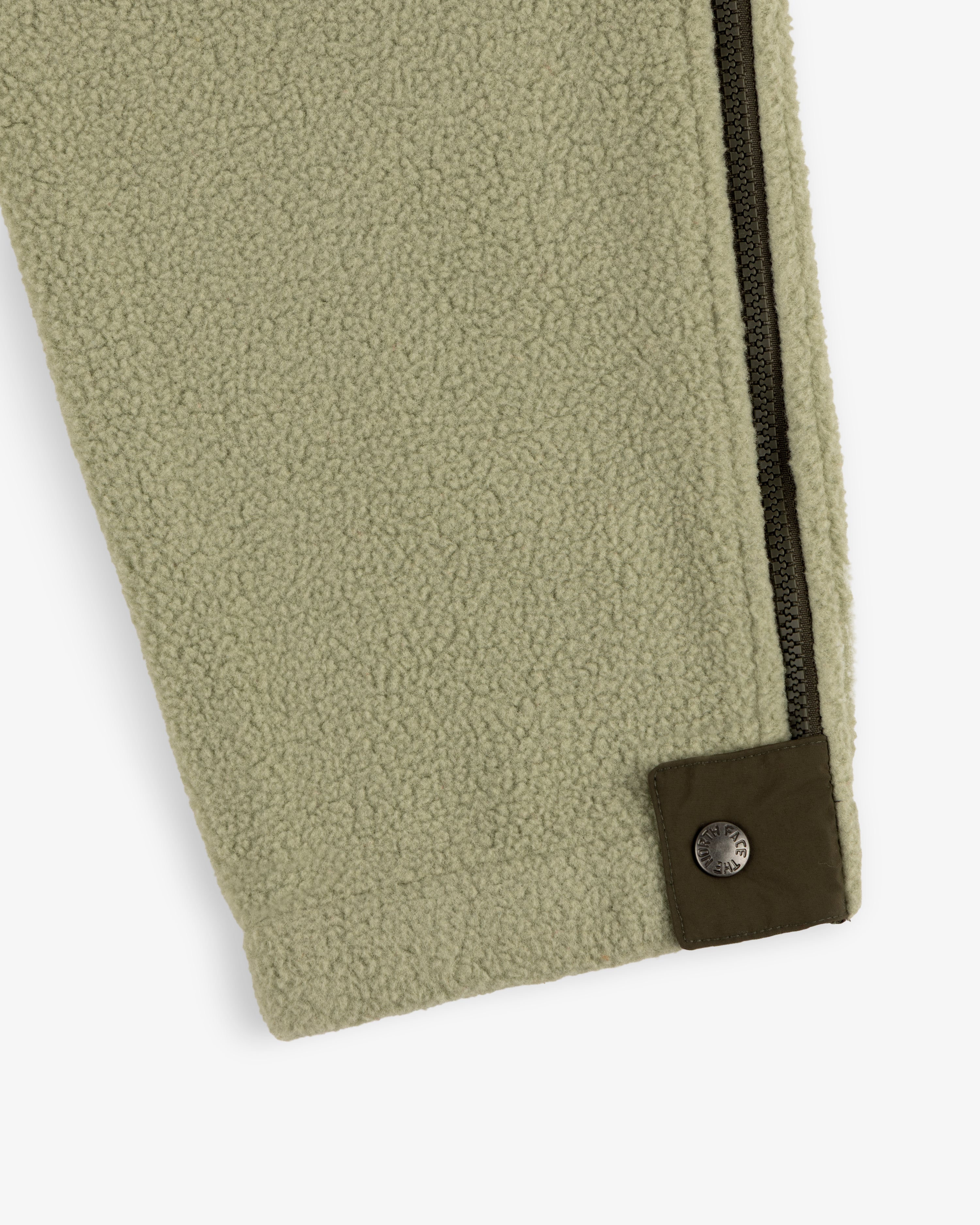 Close-up of ALD / The North Face Denali Fleece Pant in green, featuring a black zipper and dark green snap button detail.
