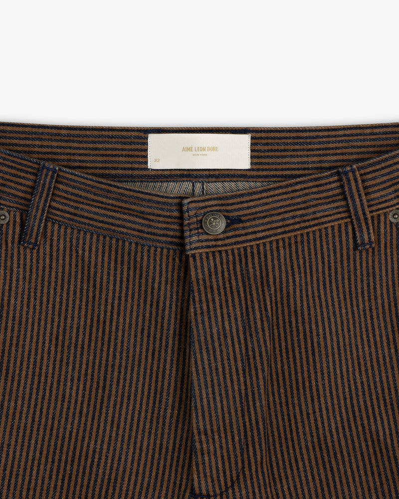 Close-up of Hickory Stripe Painter Pant featuring brown and navy stripes, button fly, and white Aime Leon Dore label.