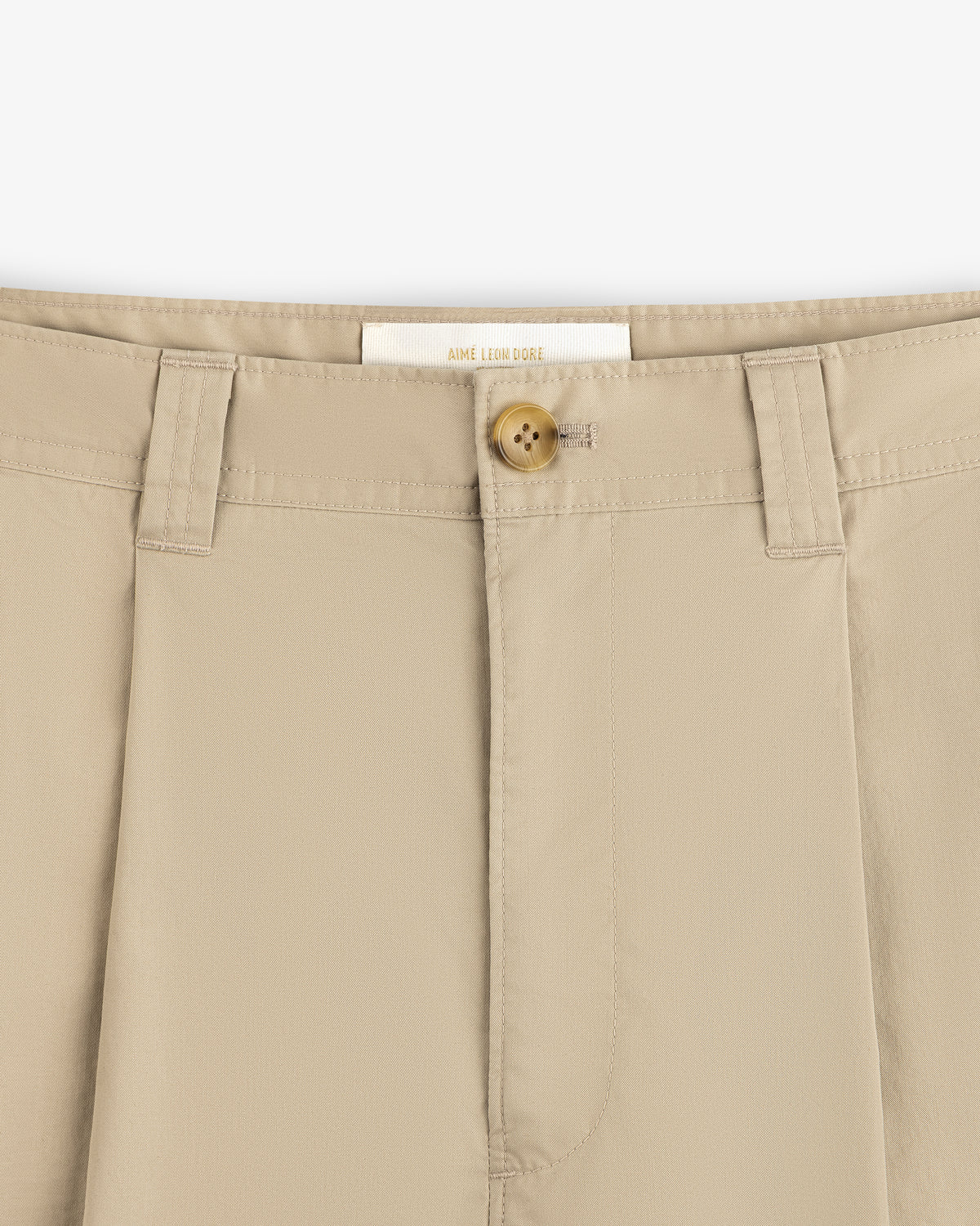 Close-up of Double Pleated Officer Pant waistband with brown button, belt loops, and visible inside label.
