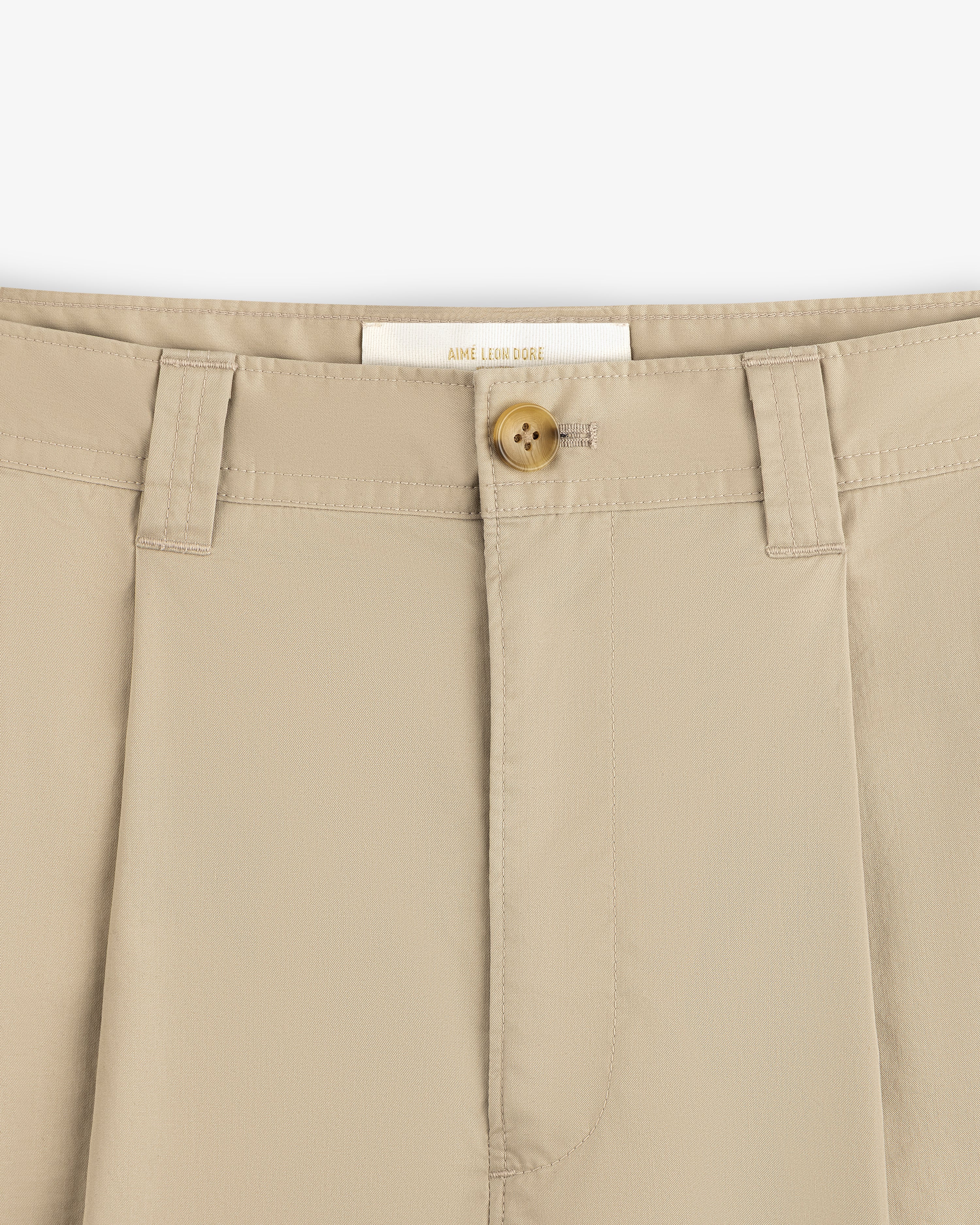 Close-up of Double Pleated Officer Pant waistband with brown button, belt loops, and visible inside label.