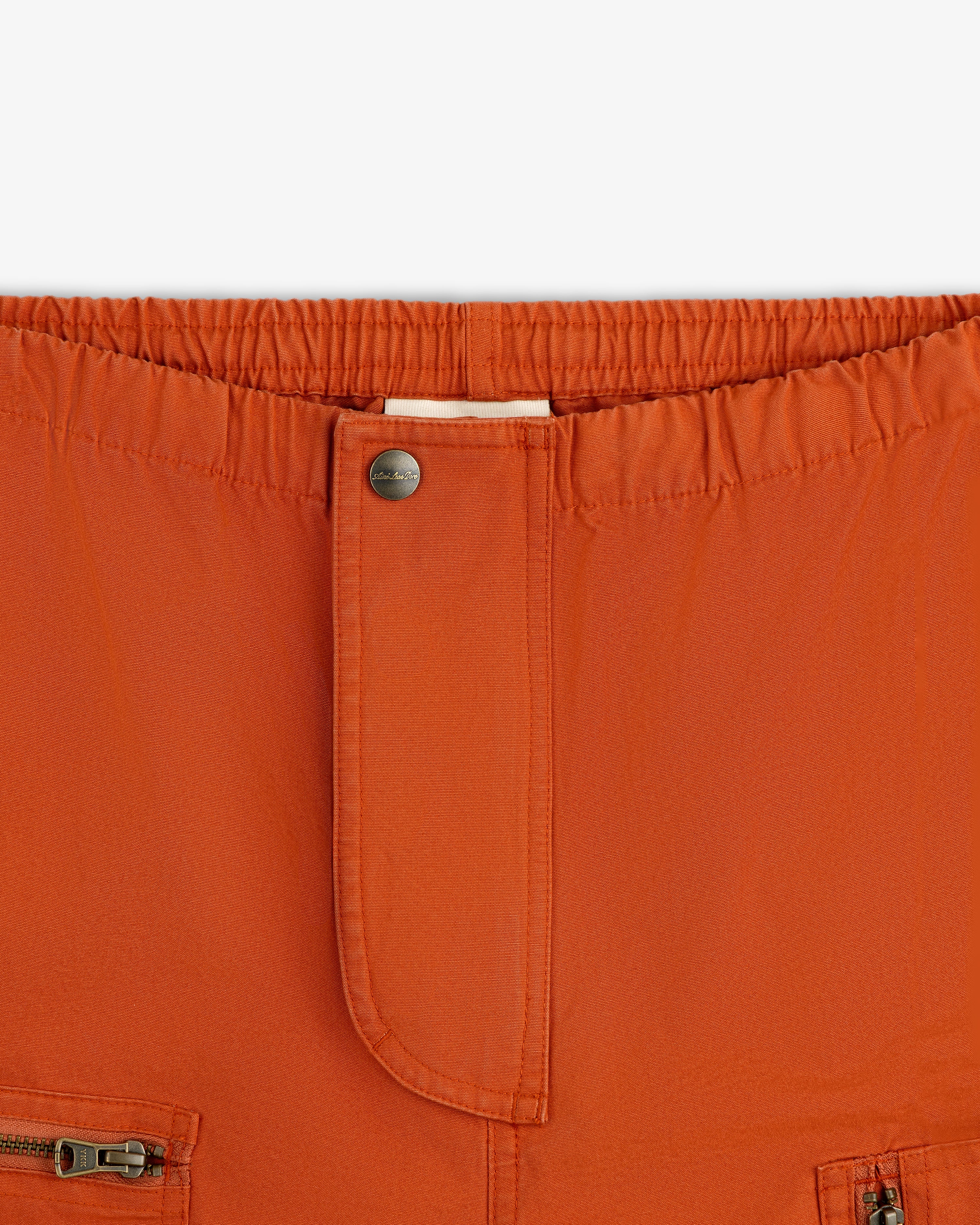 Close-up of rust-colored Garment Washed Aviator Pants with an elastic waist, front button, and zippered pockets.