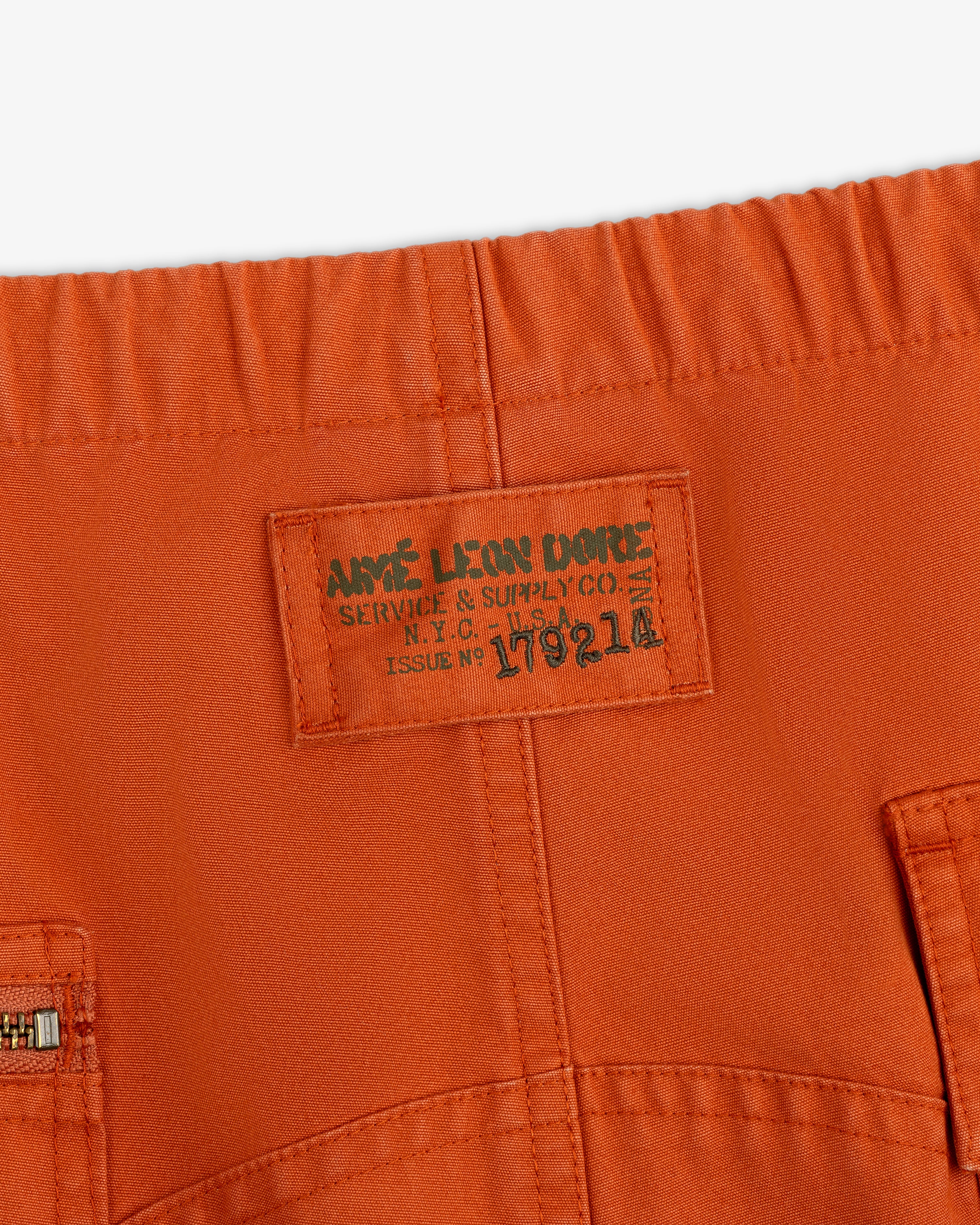 Close-up of an orange Garment Washed Aviator Pant waistband with an Aime Leon Dore Service & Supply Co. N.Y.C. U.S.A. label.