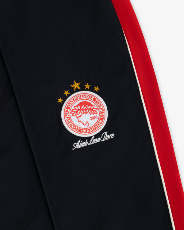 ALD / Olympiacos F.C. Nylon Track Pant in black nylon with a red side stripe and an embroidered soccer crest.
