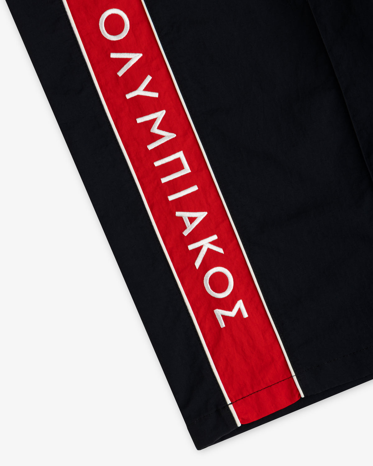 ALD / Olympiacos F.C. Nylon Track Pant in black with a vertical red side stripe and white Greek text.