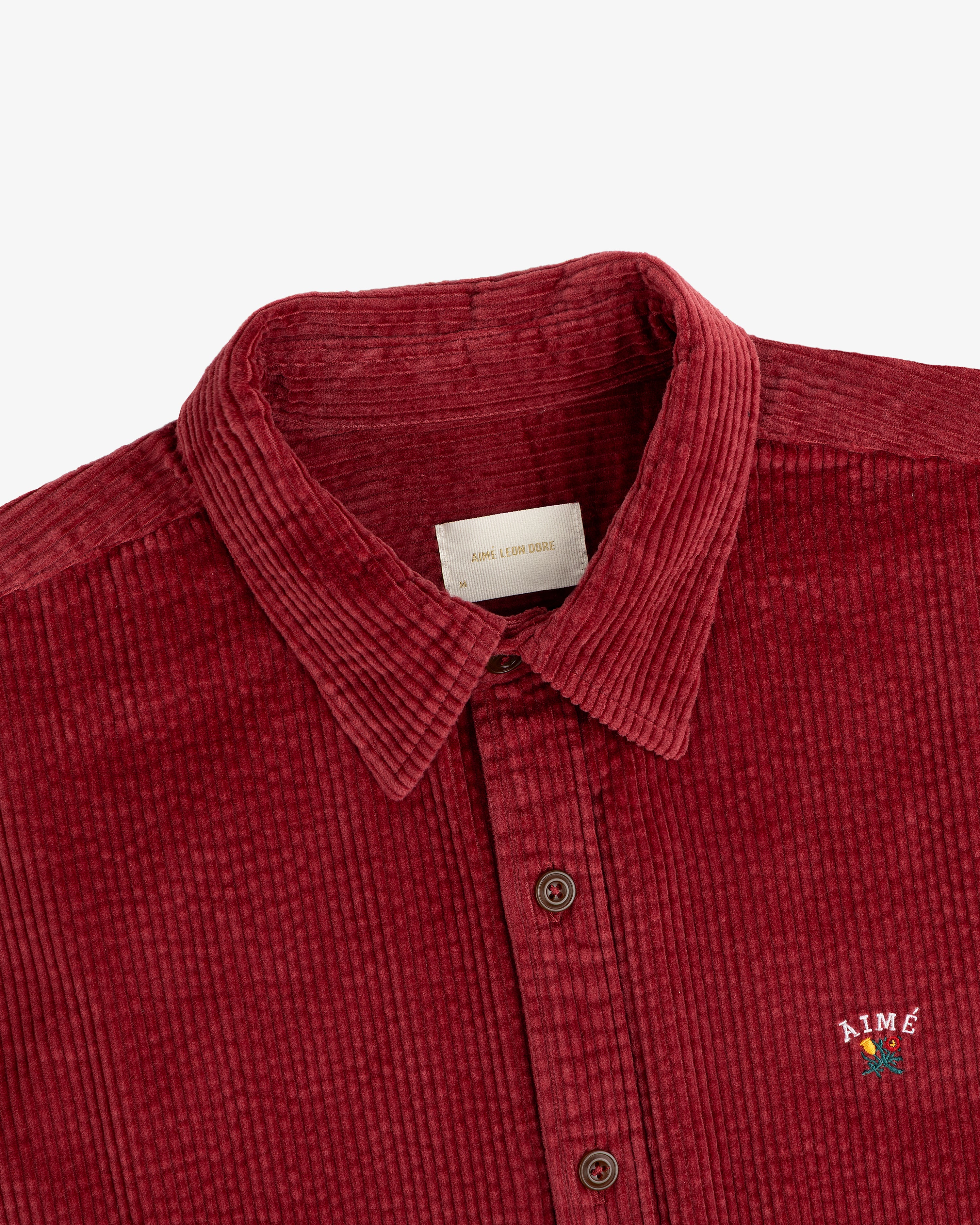 Burgundy Corduroy Leon Overshirt with a floral logo embroidered on the chest.