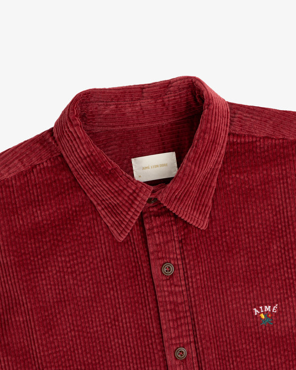 Burgundy Corduroy Leon Overshirt with a floral logo embroidered on the chest.
