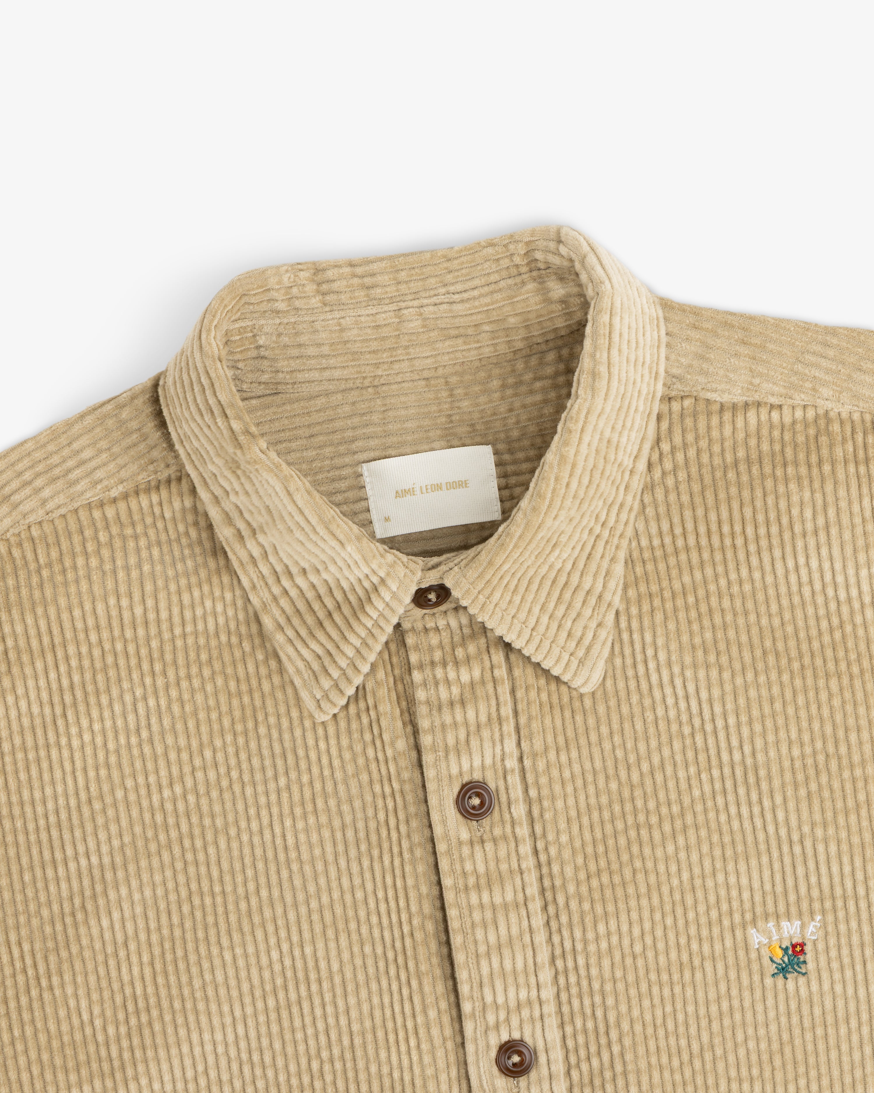 Tan Corduroy Leon Overshirt with a collar, brown buttons, and a small floral embroidery on the chest.