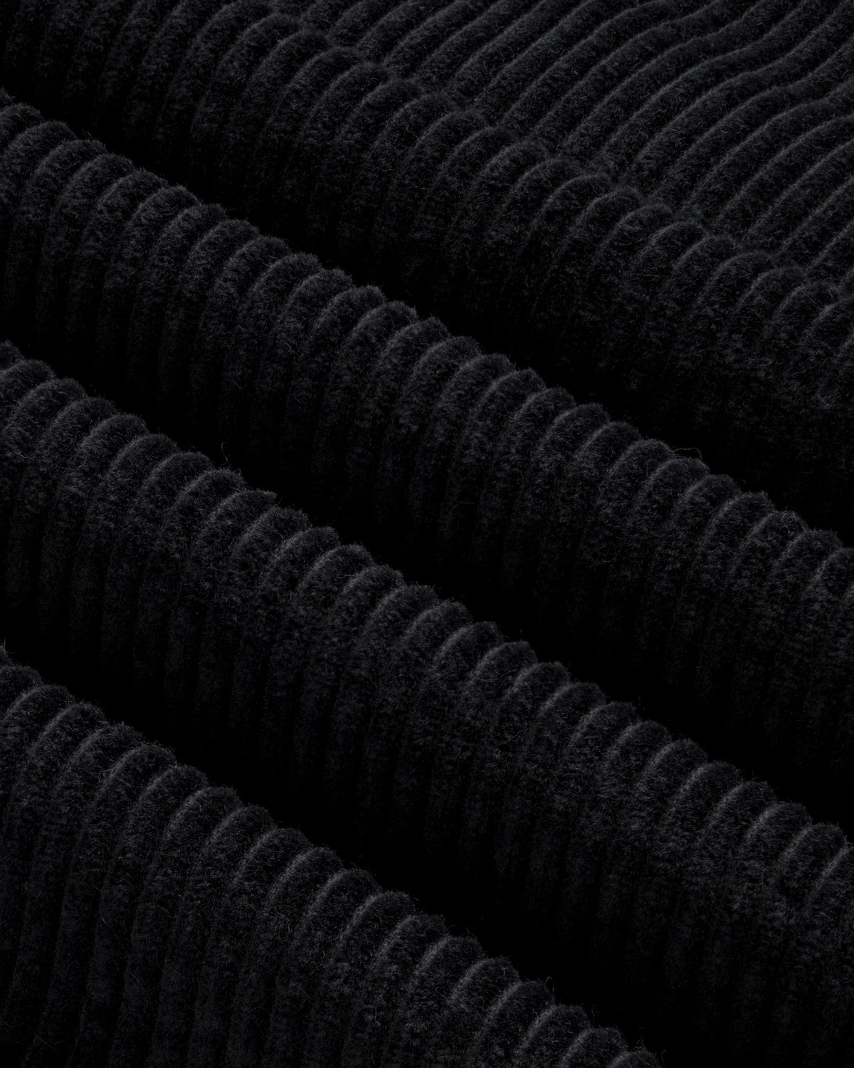 Close-up of black corduroy fabric with thick, diagonal ridges on a Quarter Zip Corduroy Shirt.