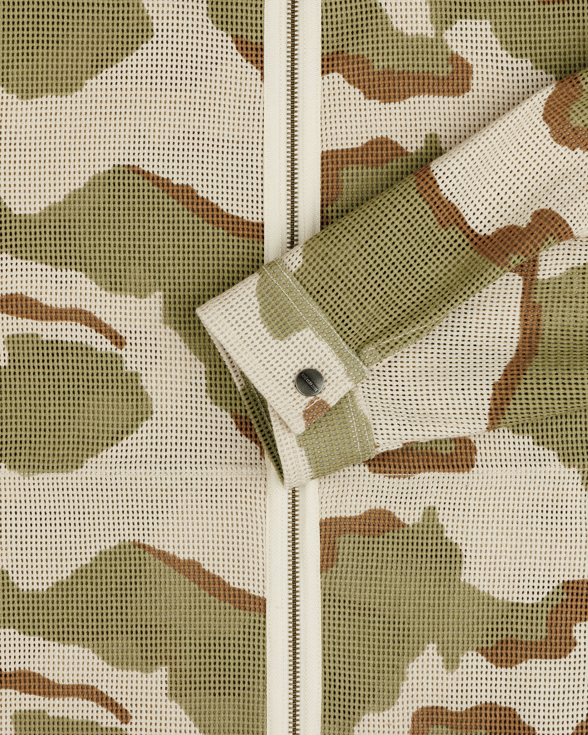 Close-up of a Camo Mesh Zip Overshirt featuring a camo-patterned mesh, zip-up closure, and a single button cuff.