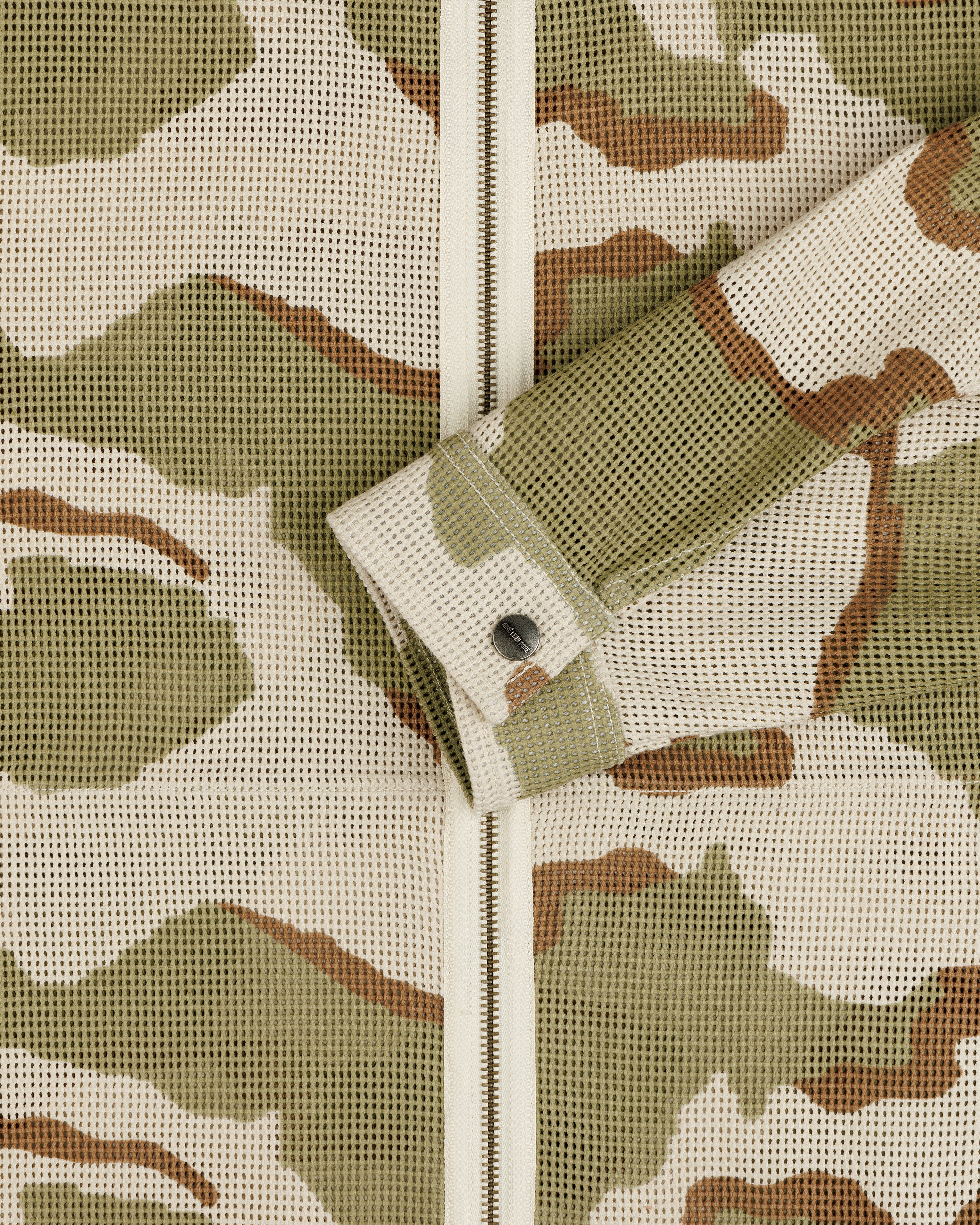 Close-up of a Camo Mesh Zip Overshirt featuring a camo-patterned mesh, zip-up closure, and a single button cuff.