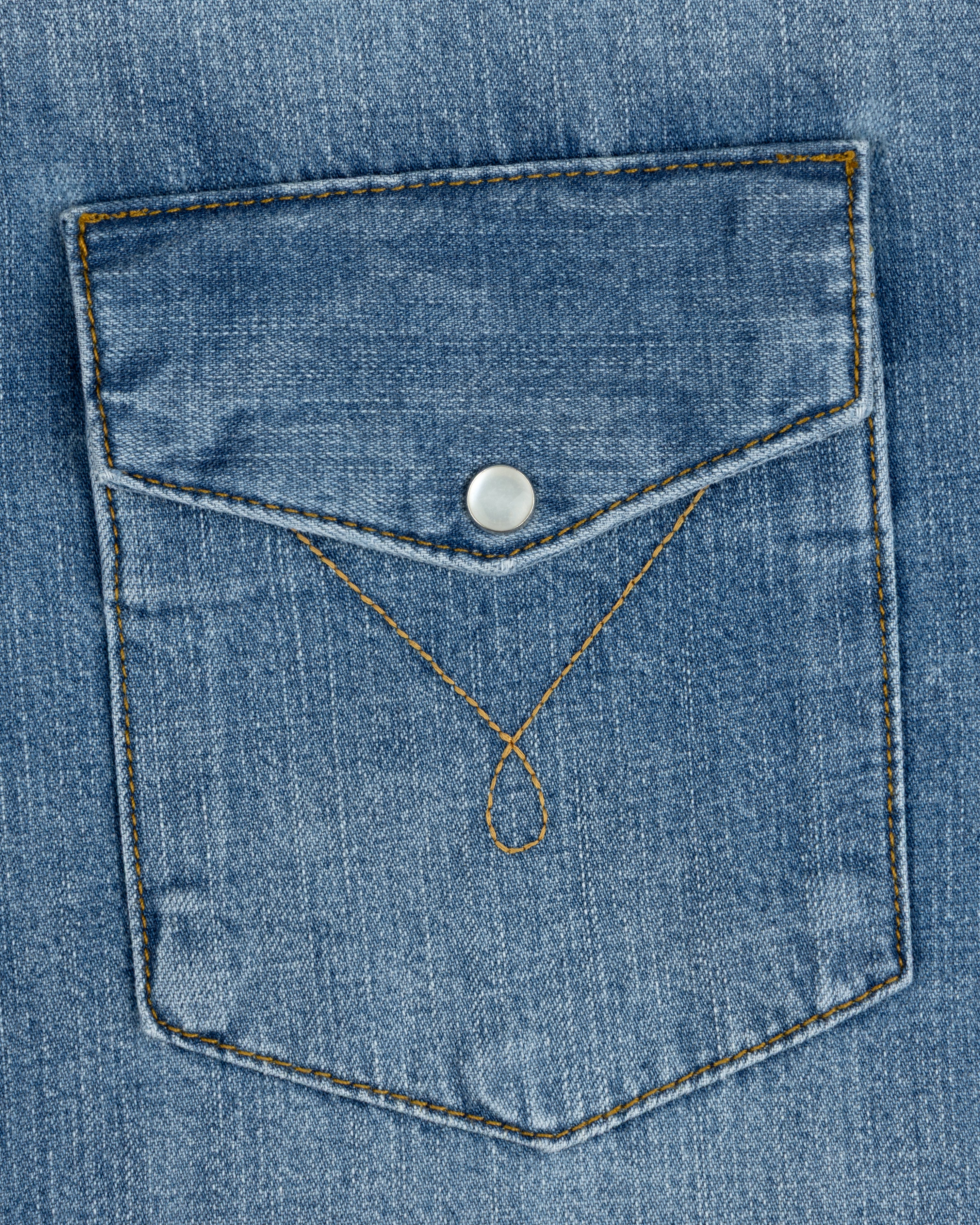 Blue denim chest pocket on a Denim Western Shirt with a pointed flap, silver snap button, and decorative gold stitching.