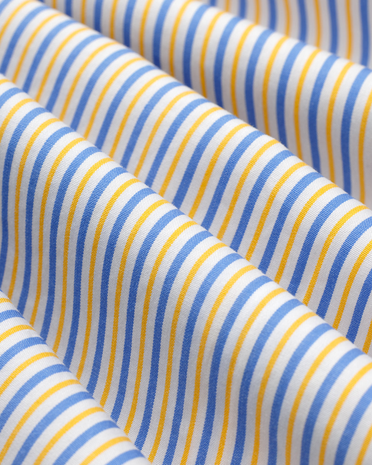 Close-up of a Striped Button Down Poplin Shirt in white fabric with thin vertical blue and yellow stripes.