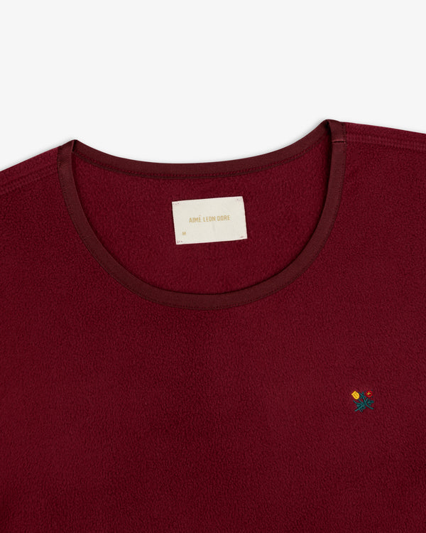 Deep red Crest Long-Sleeve Fleece Tee with a crew neckline, brand tag, and small floral embroidery.