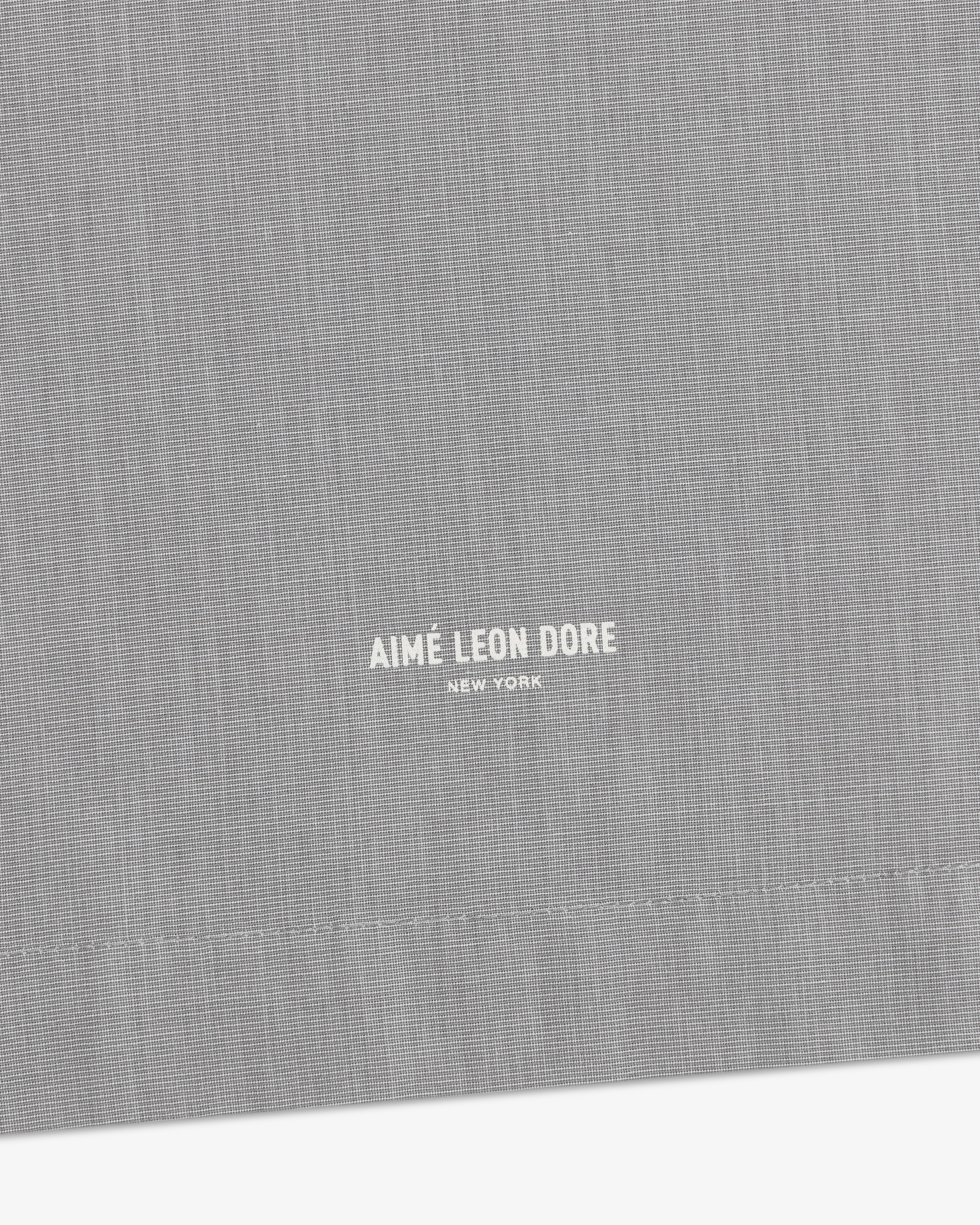 Close-up of gray Poplin Casual Shirt featuring small white Aimé Leon Dore New York text near the bottom center.