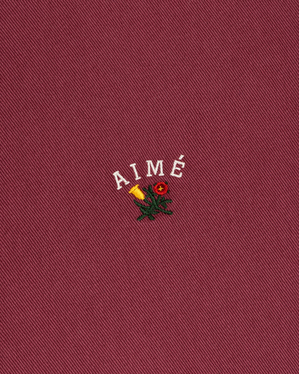 Garment Dyed Leon Overshirt: red with white AIMÉ text, yellow rose, and green leaves embroidery.