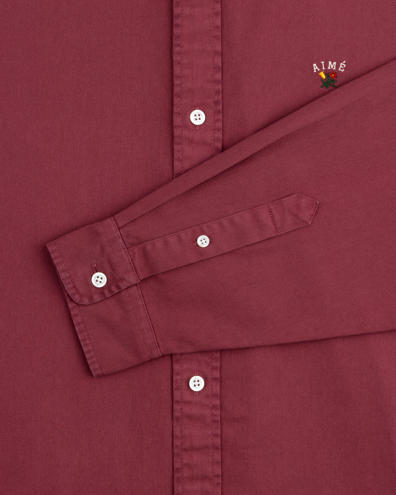Garment Dyed Leon Overshirt in maroon with white buttons, visible sleeve, and AIMÉ flower embroidery.