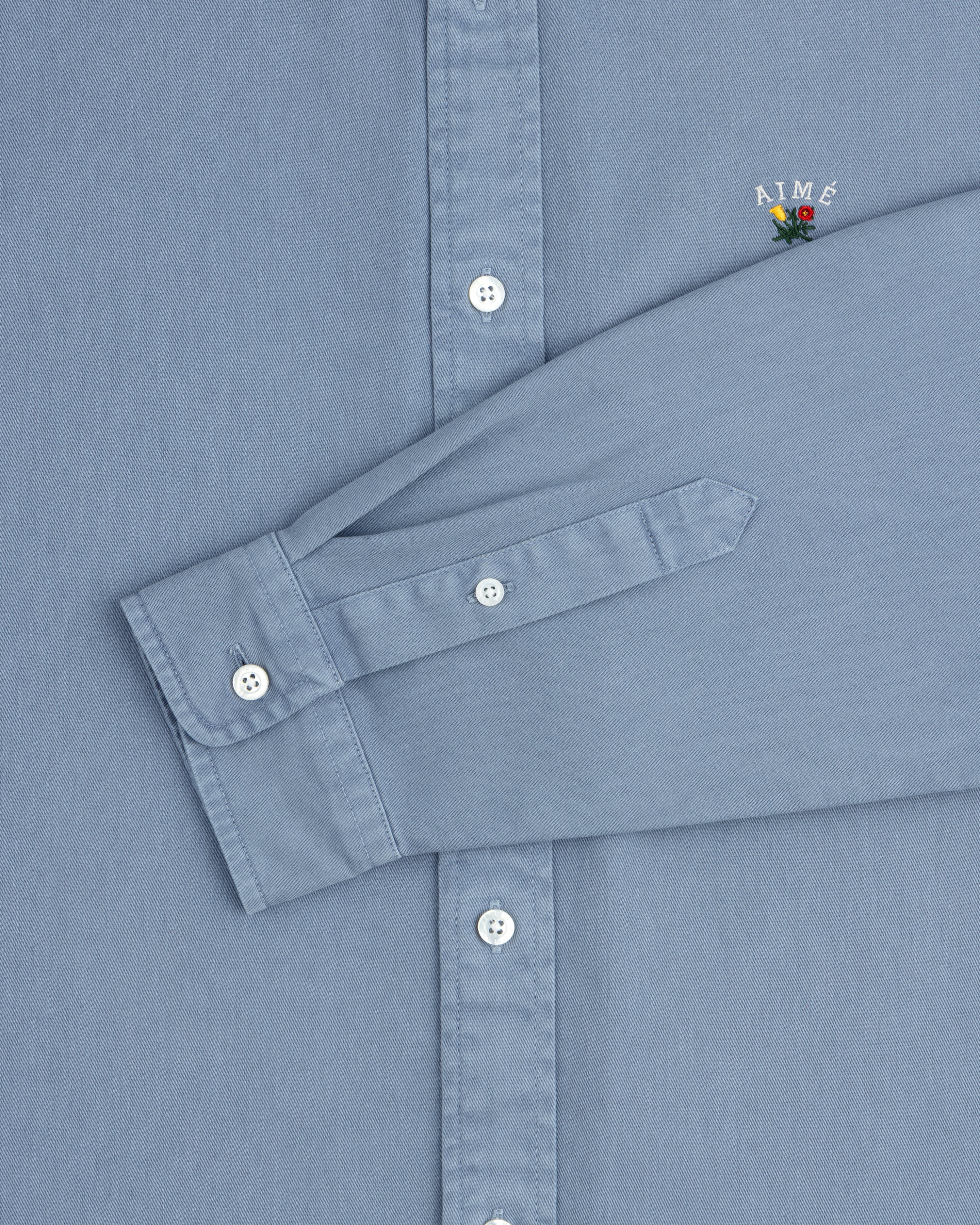 Garment Dyed Leon Overshirt: light blue, white buttons, small AIMÉ embroidery above the cuff.