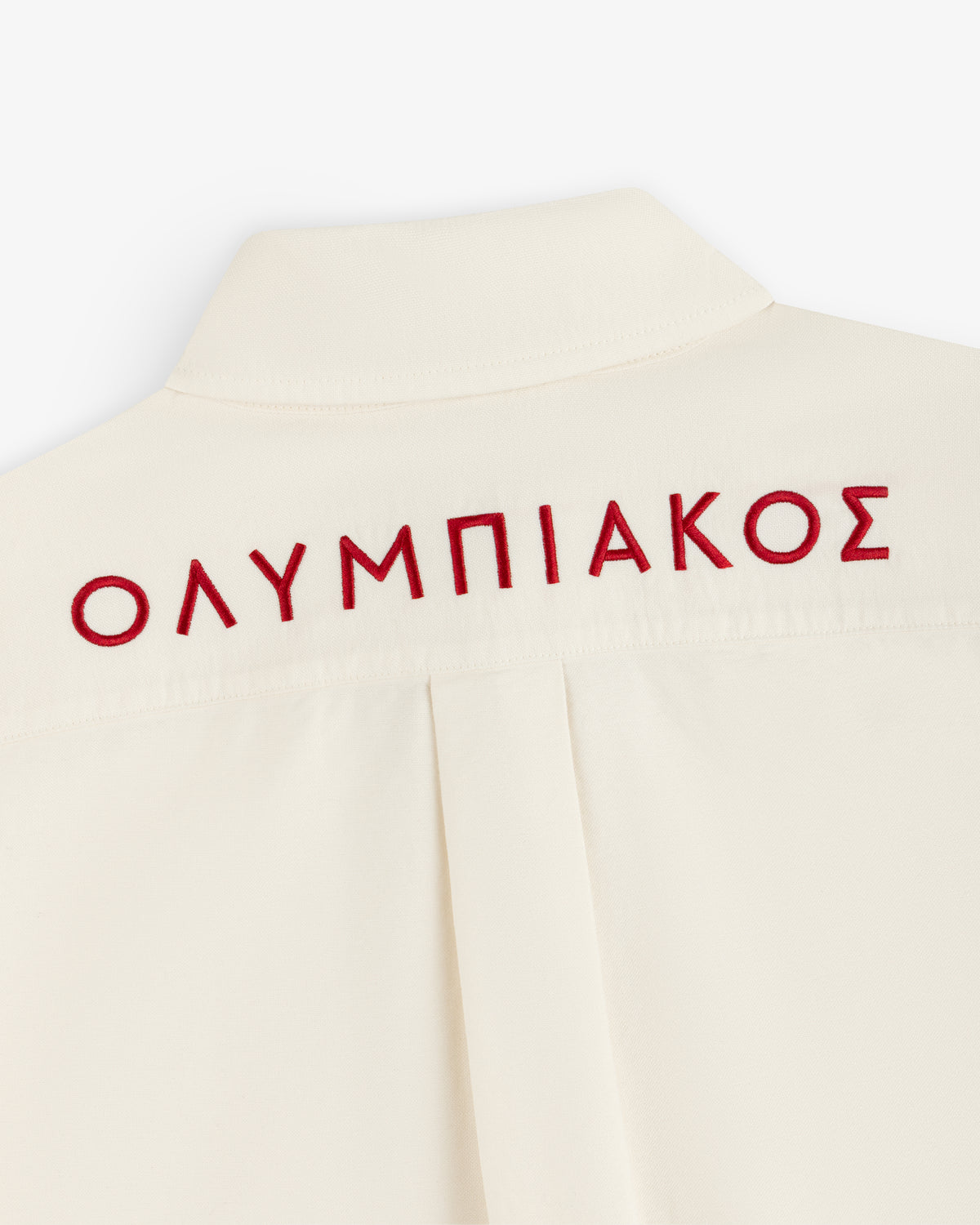 Cream-colored ALD / Olympiacos F.C. Logo Oxford Shirt with the Greek word ΟΛΥΜΠΙΑΚΟΣ embroidered in red on the back.