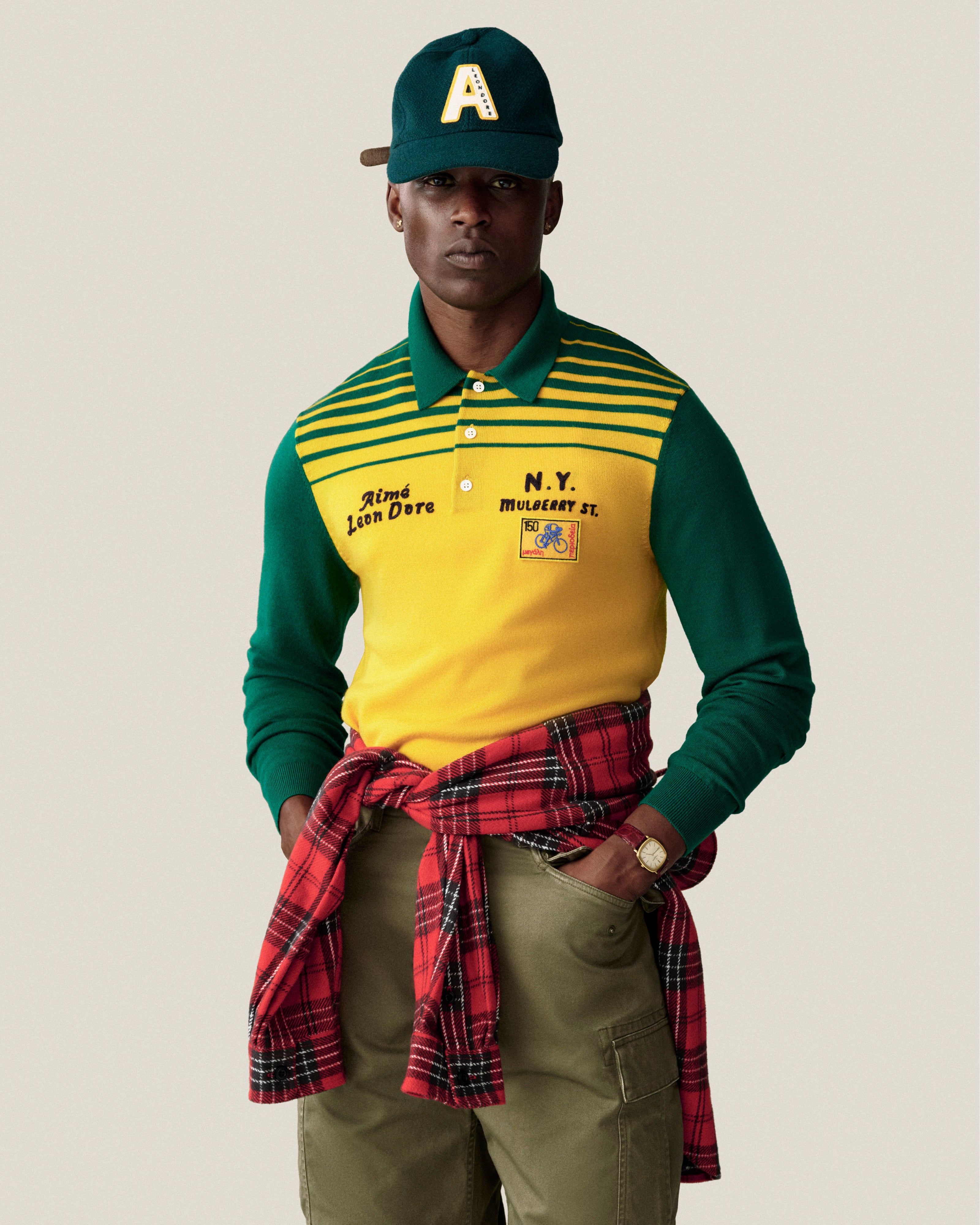 A man wears a green Wool Varsity Logo Hat, a yellow and green long-sleeve polo shirt, and green pants.