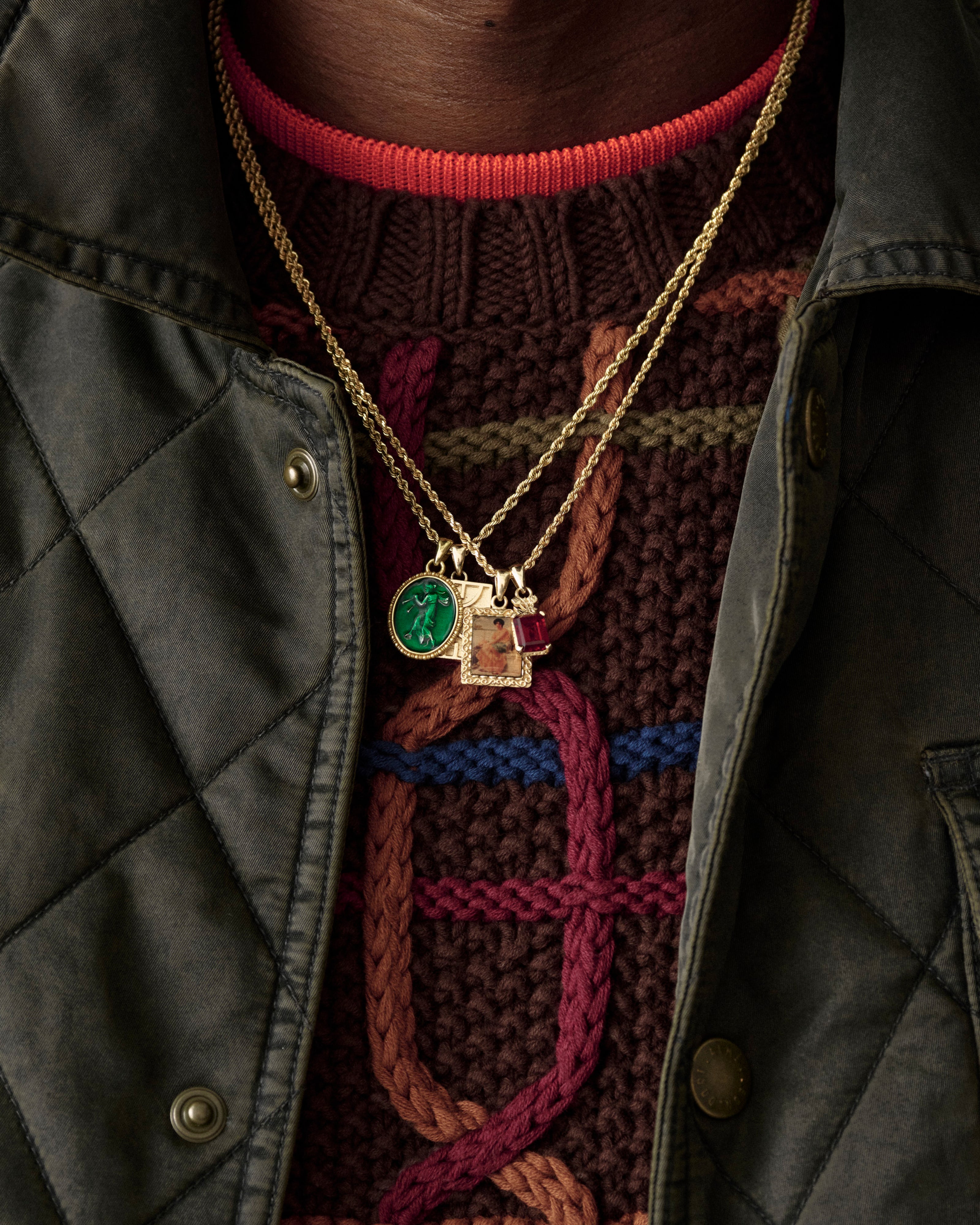 Close-up of a 14Kt Gold Crest Gemstone Pendant over a brown cable-knit sweater and green quilted jacket.