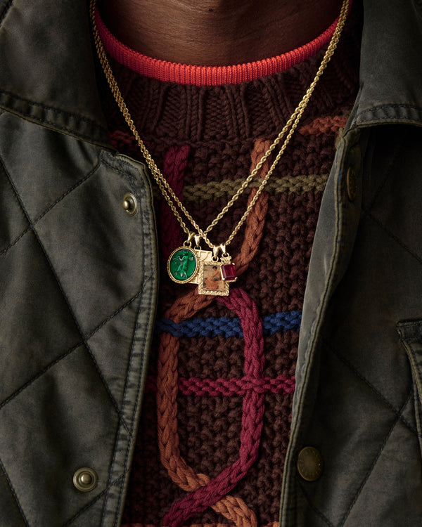 Close-up of a 14Kt Gold Crest Gemstone Pendant over a brown cable-knit sweater and green quilted jacket.