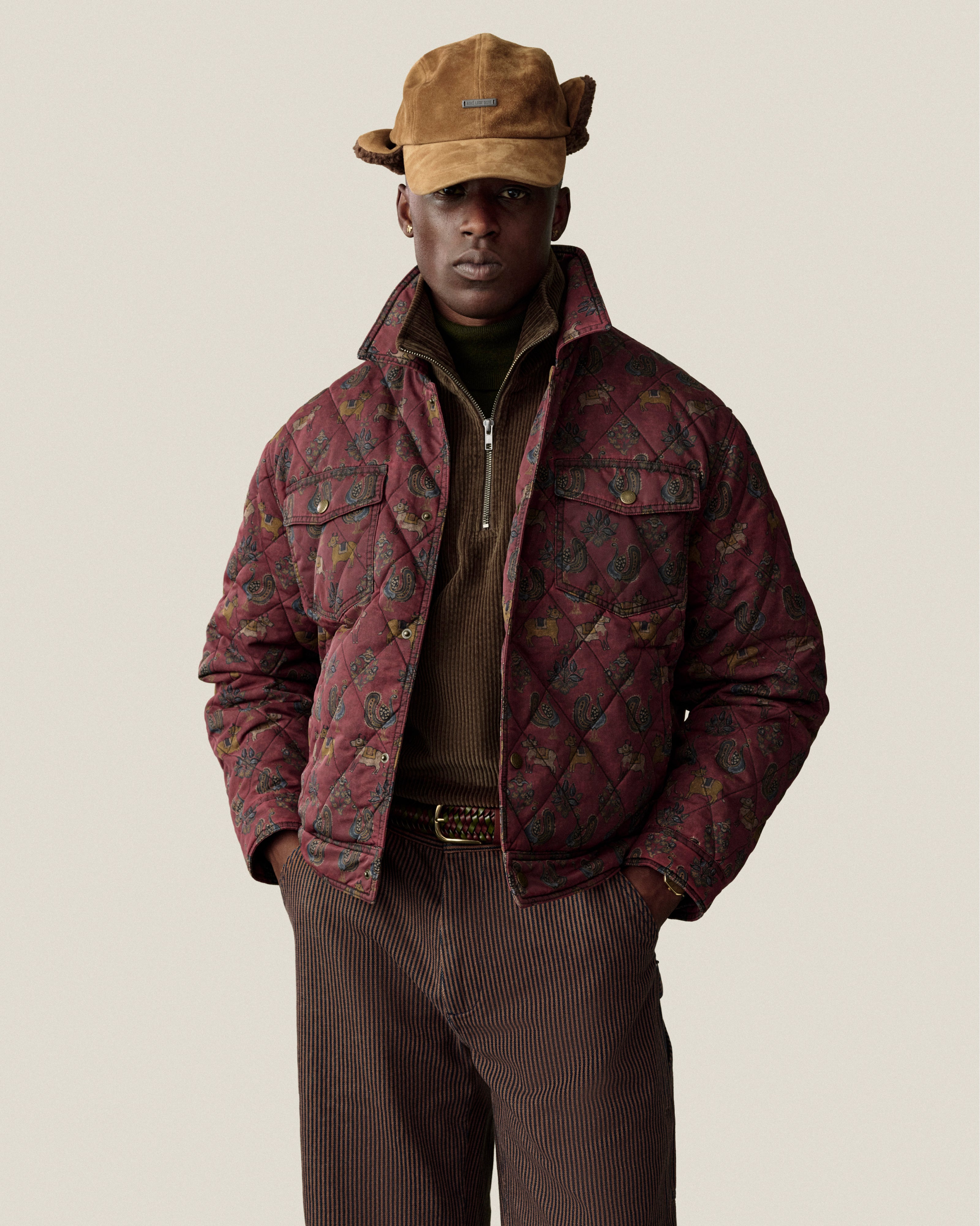 A person wears a brown Quarter Zip Corduroy Shirt under a quilted, patterned maroon jacket and brown trousers.
