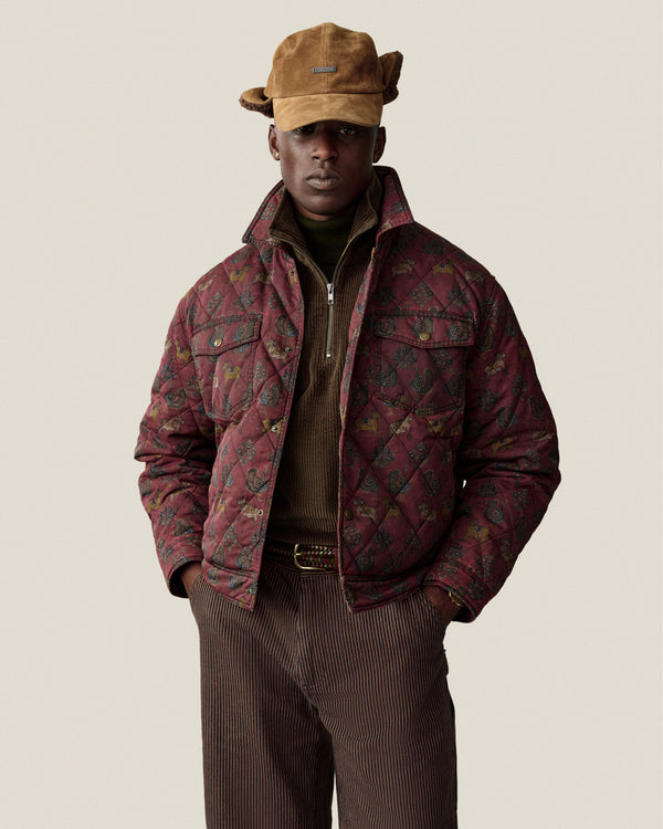 A person wears a brown Quarter Zip Corduroy Shirt under a quilted, patterned maroon jacket and brown trousers.
