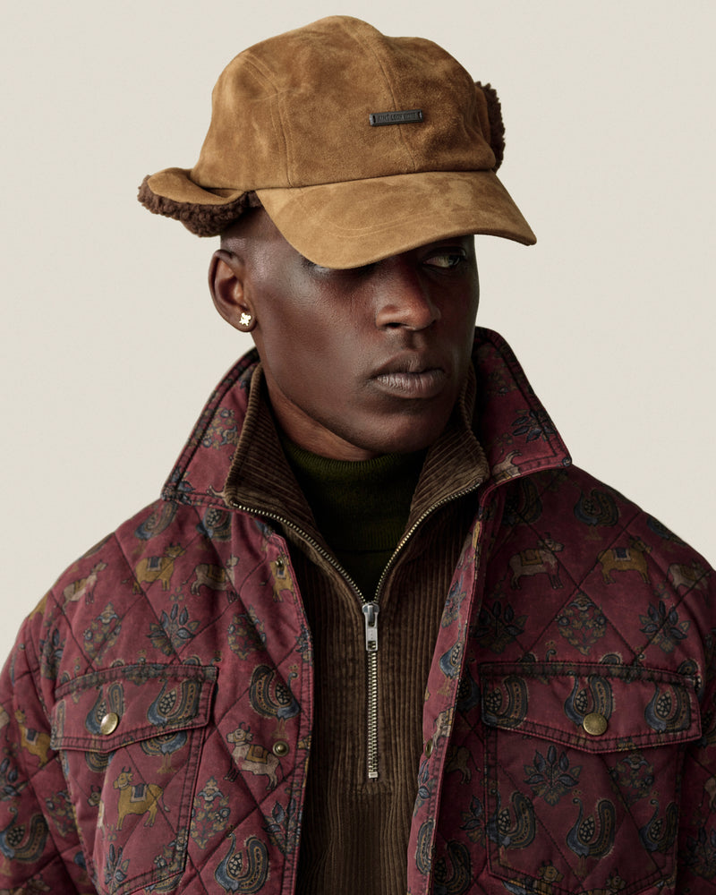 Man wearing a tan Shearling Earflap Hat and a quilted jacket with a floral and animal print.