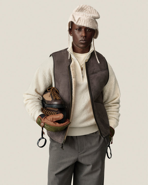 A person in an Alpaca Wool Quarter Zip Sweater holds boots and gloves, posing against a plain light background.
