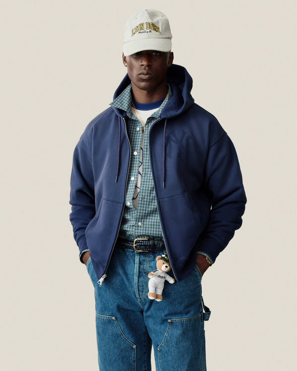 Man in Plaid Casual Shirt, blue hoodie, jeans, cap, and teddy bear keychain on his belt.
