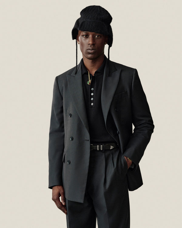 A person wearing a black Alpaca Wool Knit Earflap Hat, a black polo shirt, and a dark double-breasted blazer.