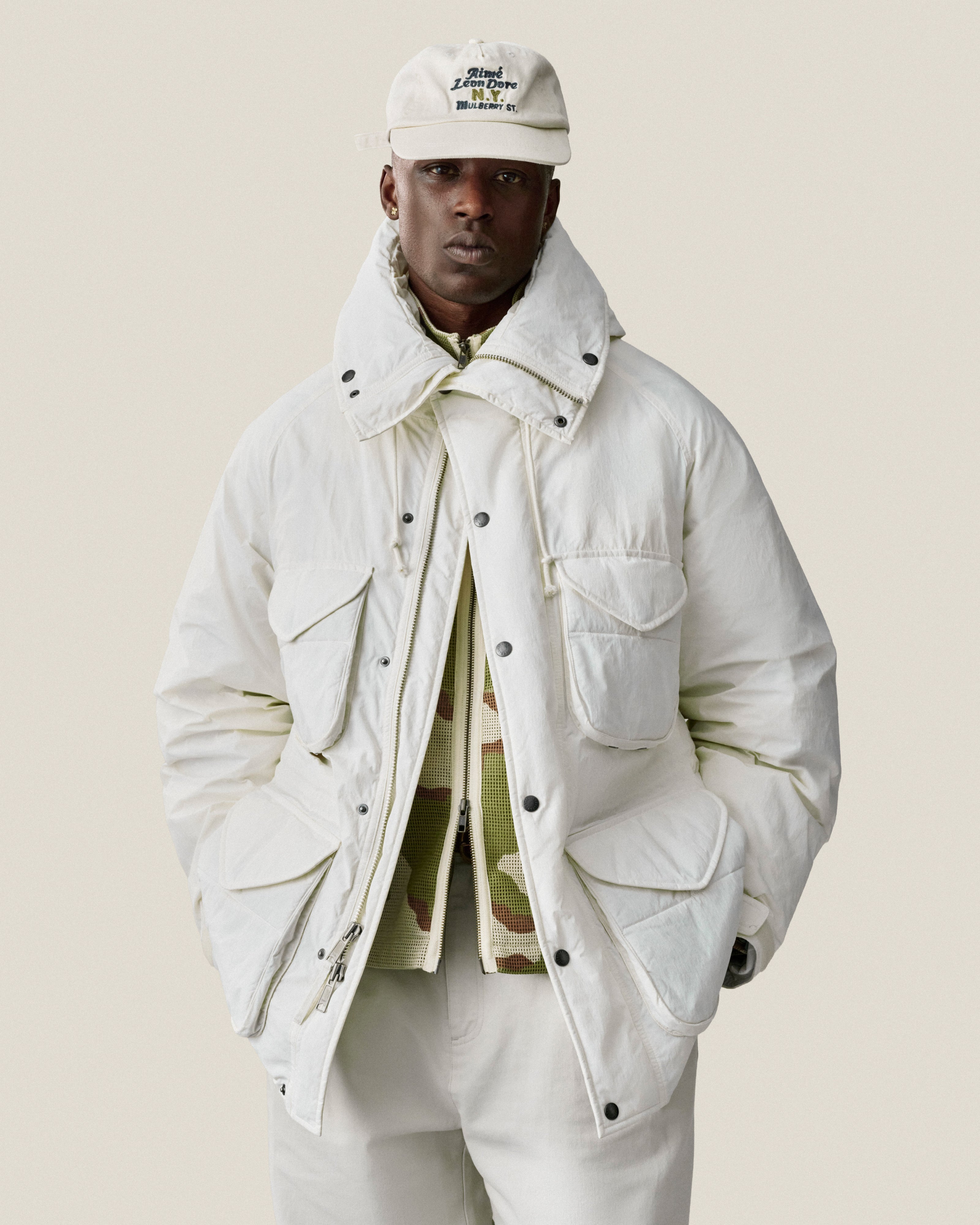 Man wearing a Mulberry Chainstitch Hat, white jacket, and pants, posing with hands in pockets against a light background.