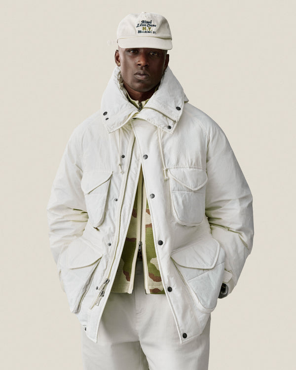 Man wearing a Mulberry Chainstitch Hat, white jacket, and pants, posing with hands in pockets against a light background.