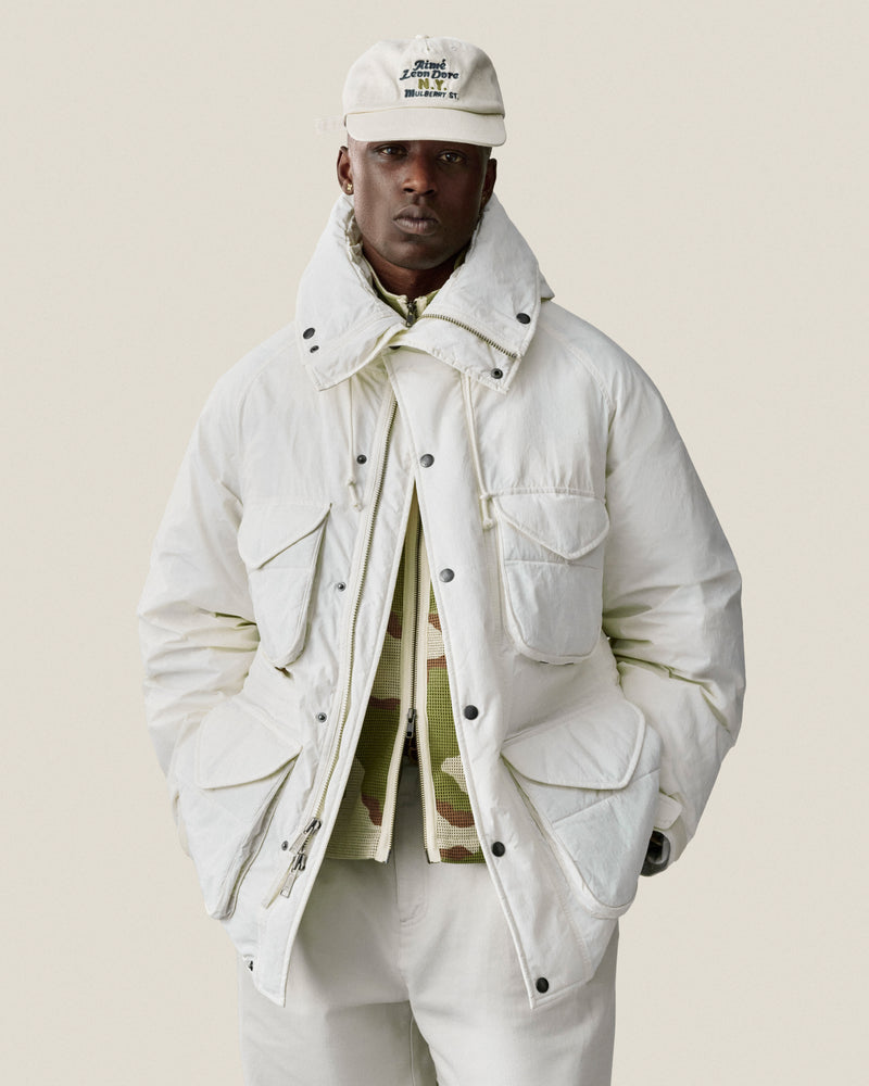 Man wearing a Mulberry Chainstitch Hat, white jacket, and pants, posing with hands in pockets against a light background.