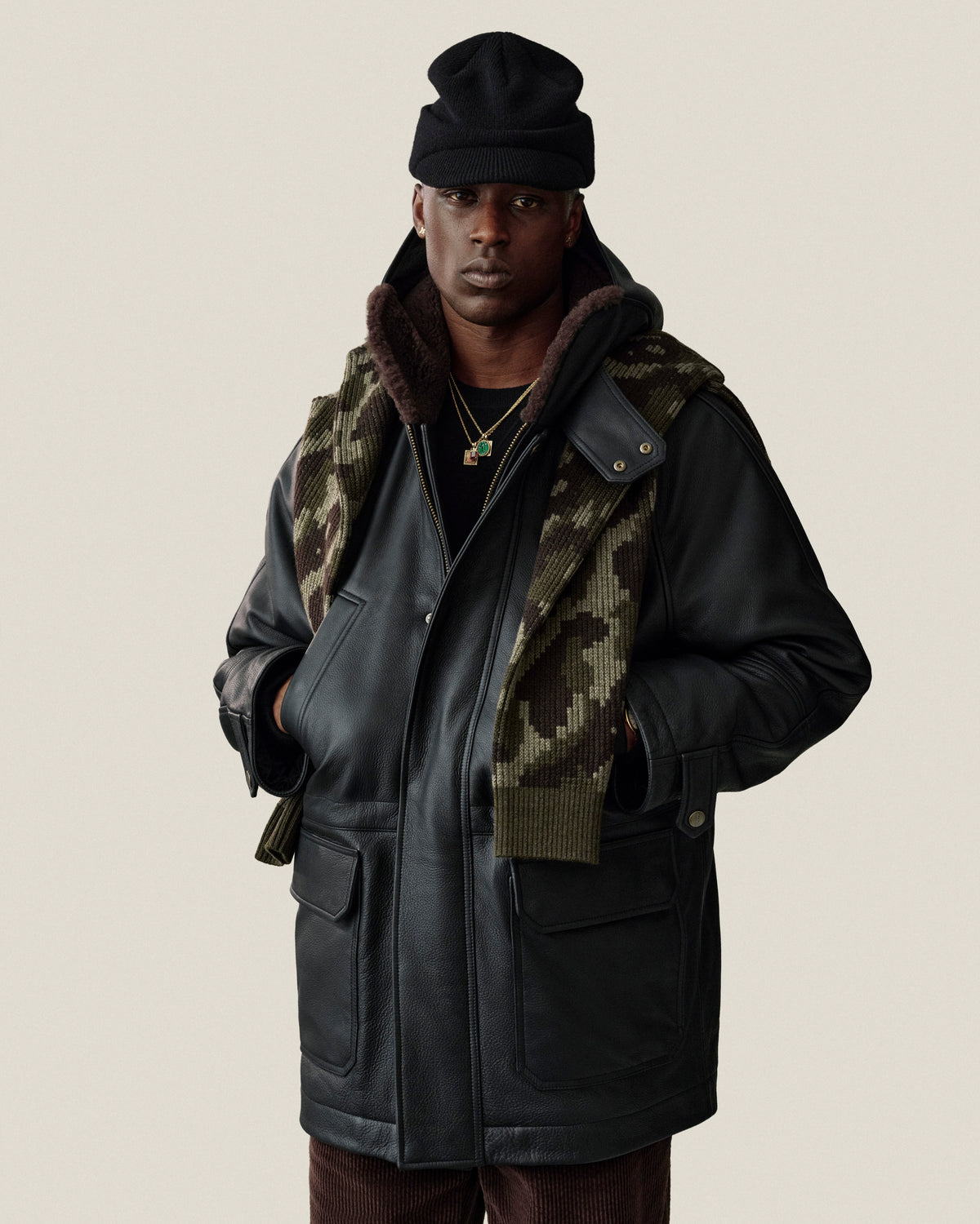 A person wearing a black Wool Brim Beanie, a black shearling-lined leather jacket, and a camouflage print scarf.